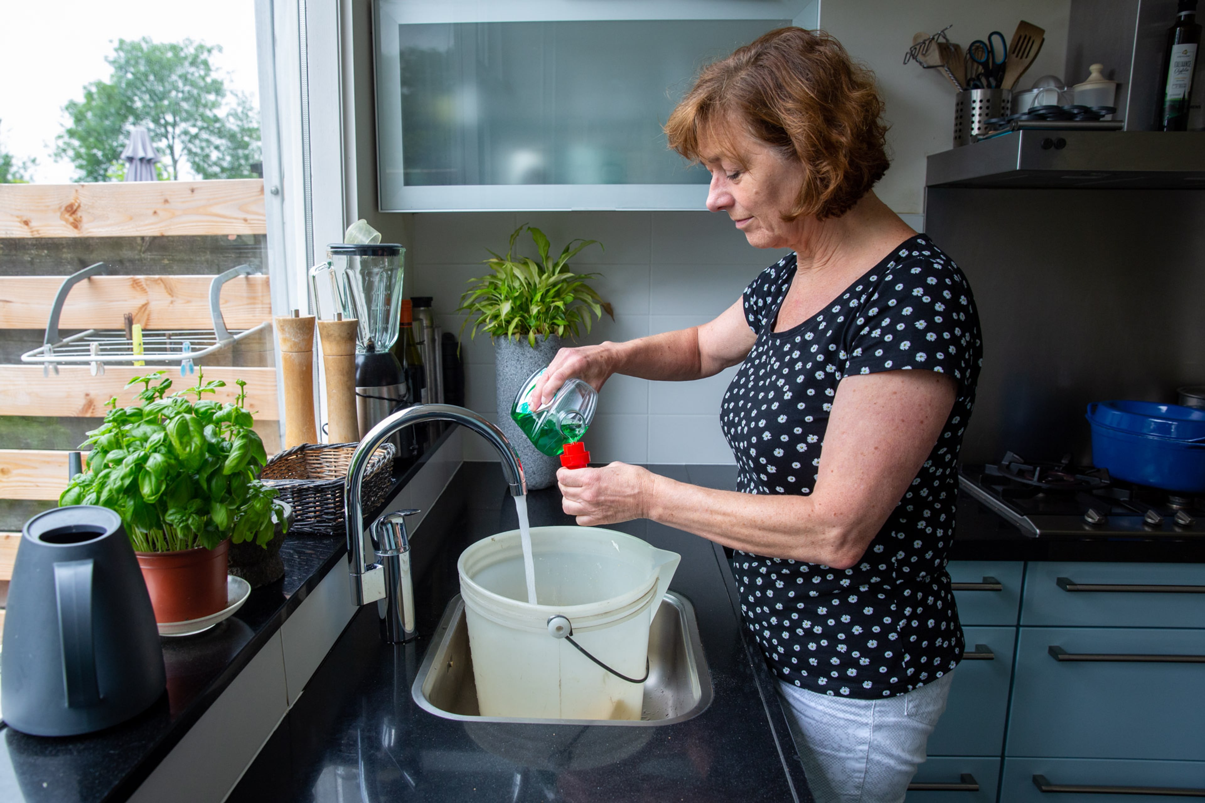Vrouw schenkt schoonmaakmiddel in doseerdop. Gebruik niet te veel schoonmaakmiddel