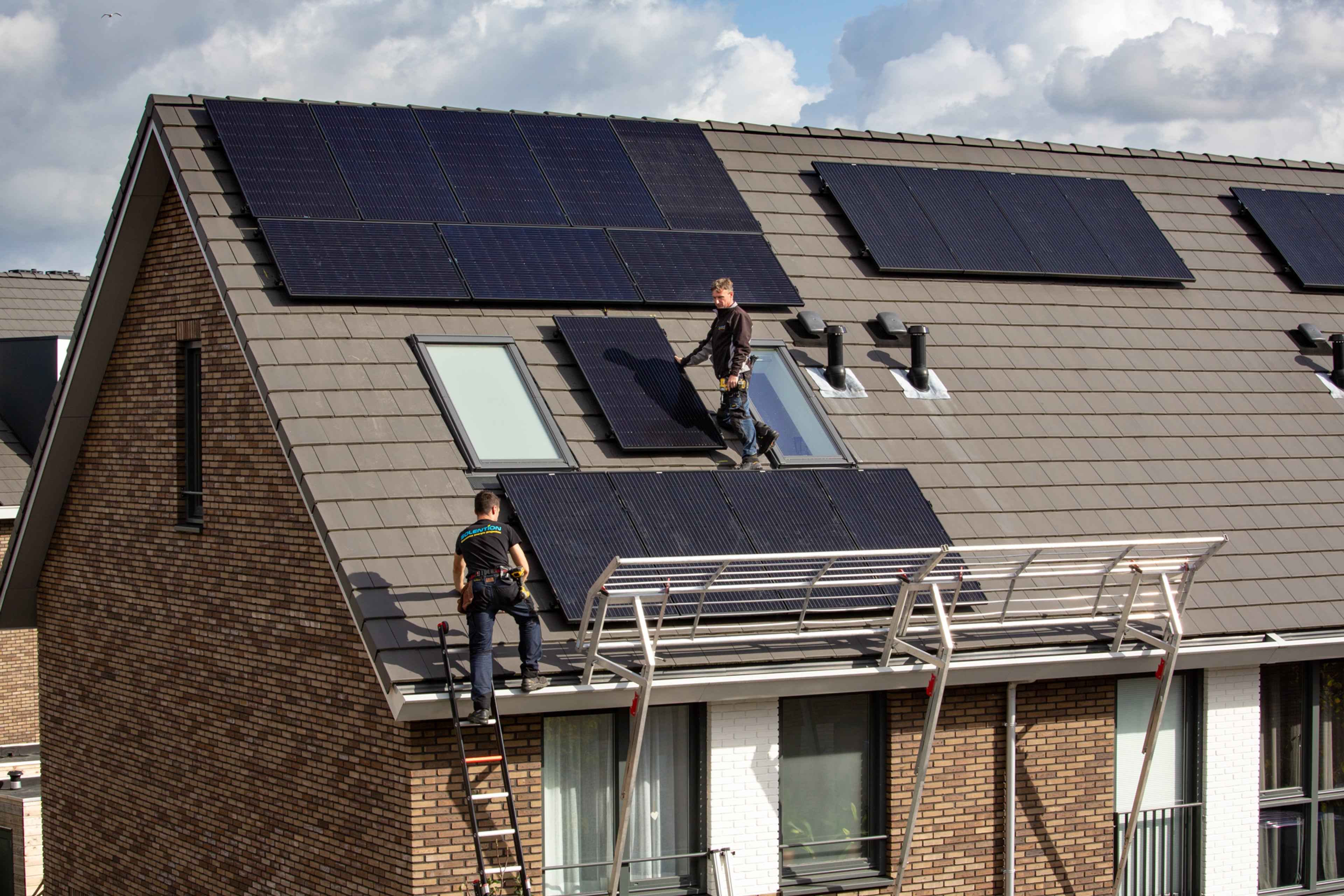 Twee installateurs monteren zonnepanelen op dak rijtjeshuis.