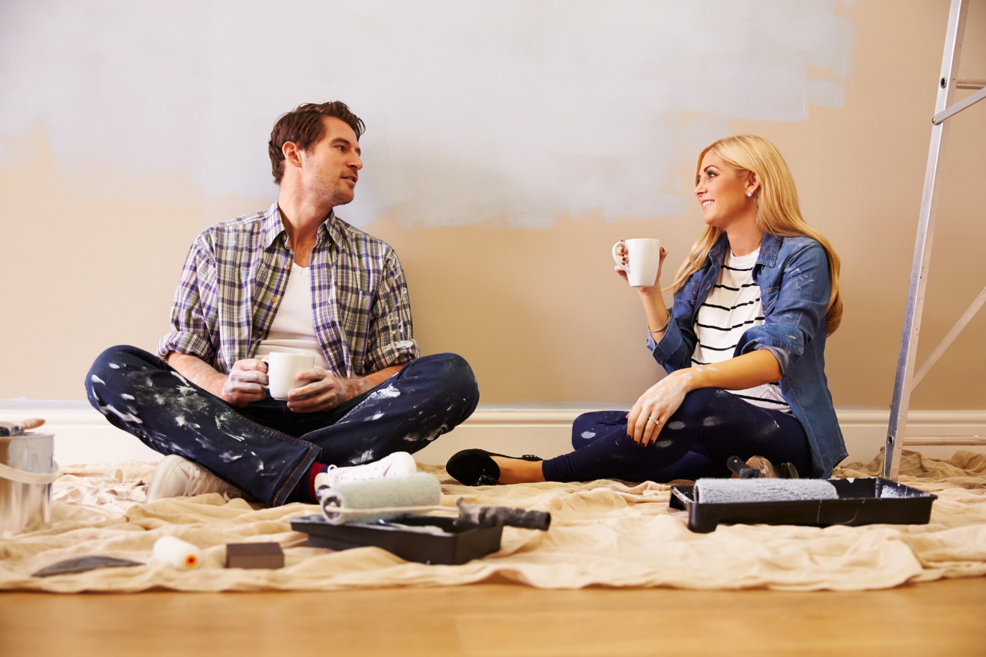 Man en vrouw drinken temidden van verfspullen zittend op de grond een kop verse koffie. Gezond in en om huis en schilderen van hout.