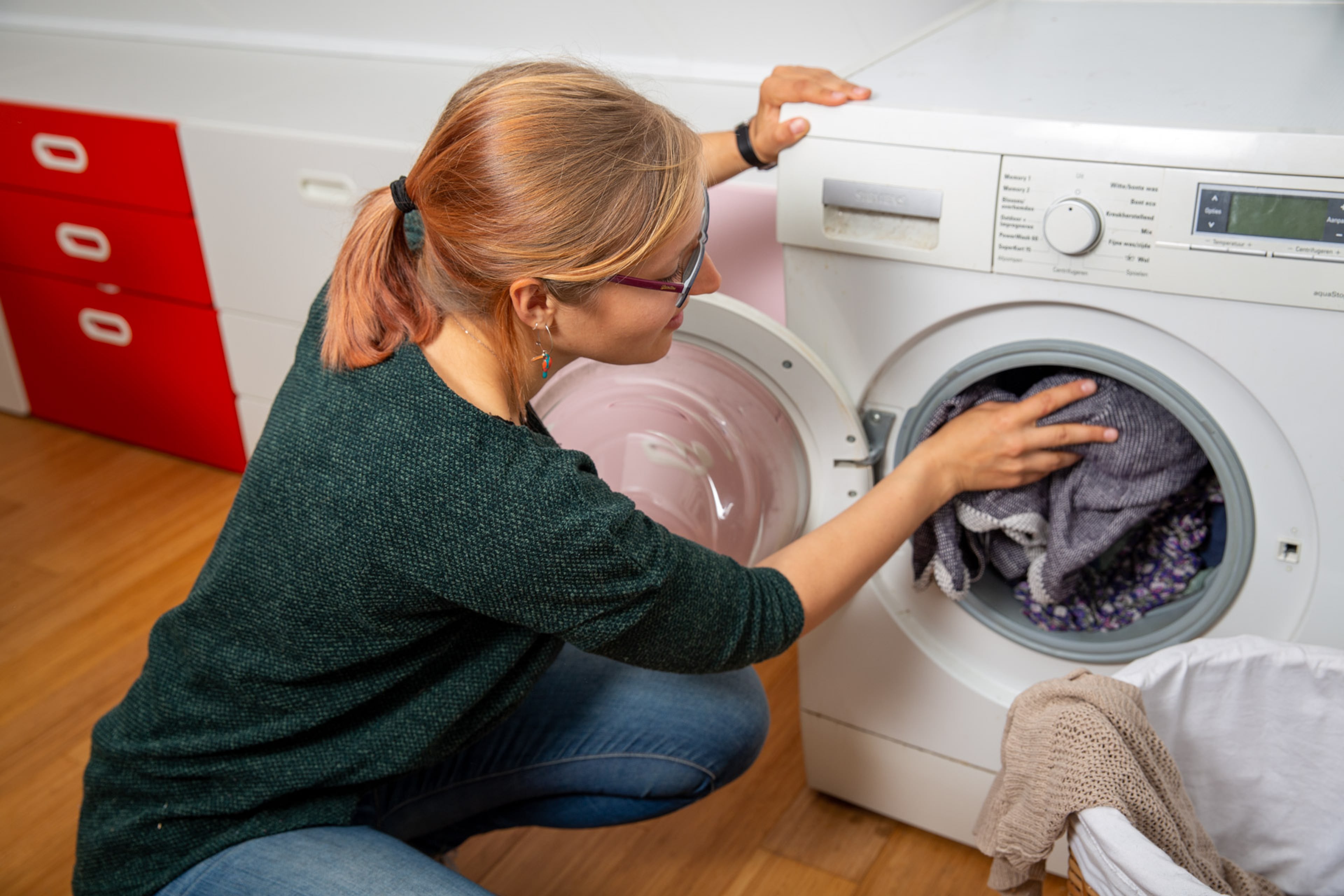 Jonge vrouw stopt de was in de wasmachine.