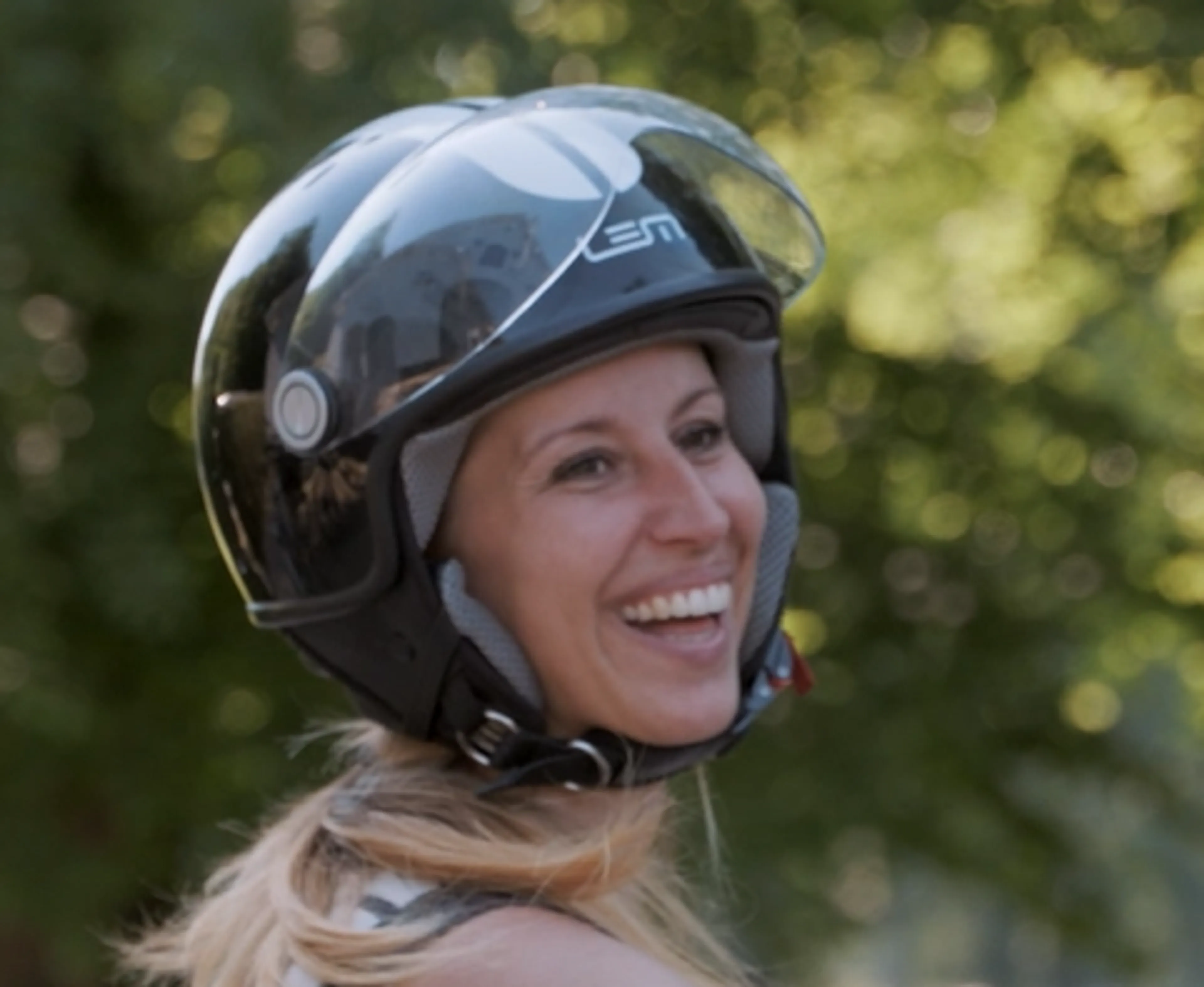 Foto van een lachende, blonde vrouw met een scooterhelm op.