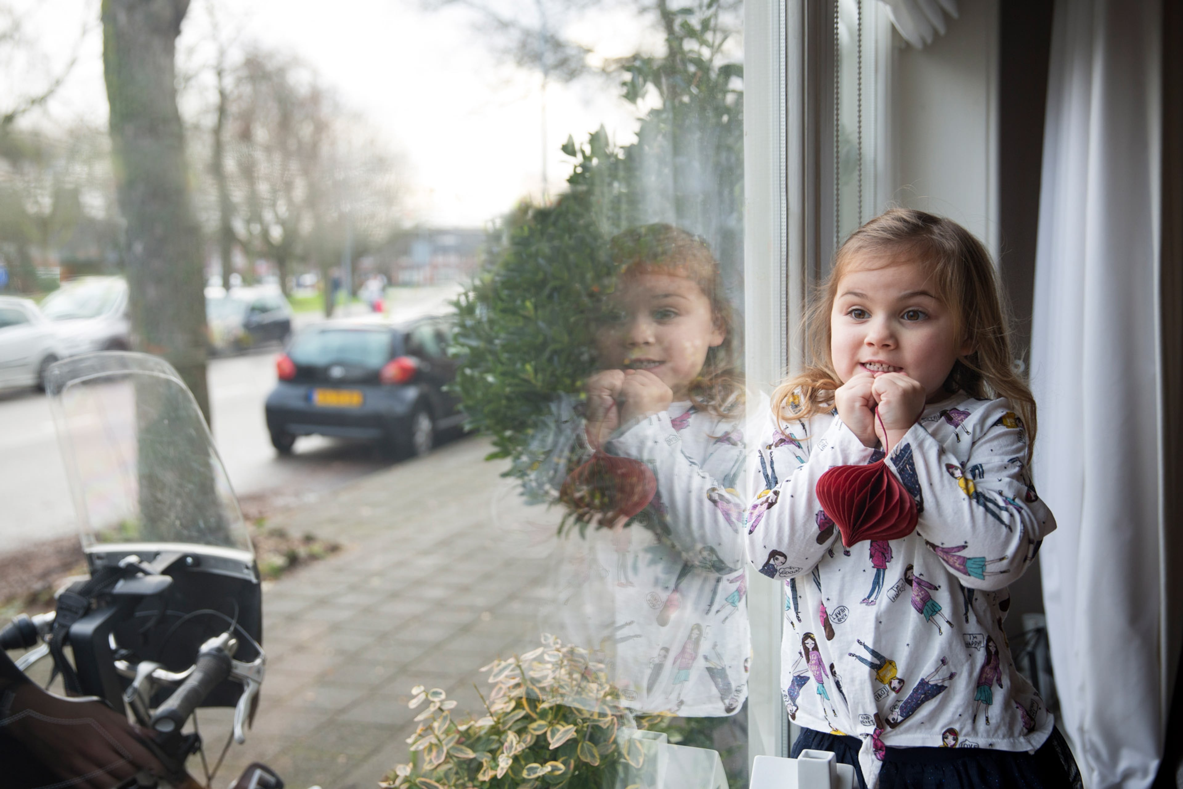 Meisje staat bij raam. Met isolerend glas en kozijnen is het lekker warm in huis en bespaar je energie.