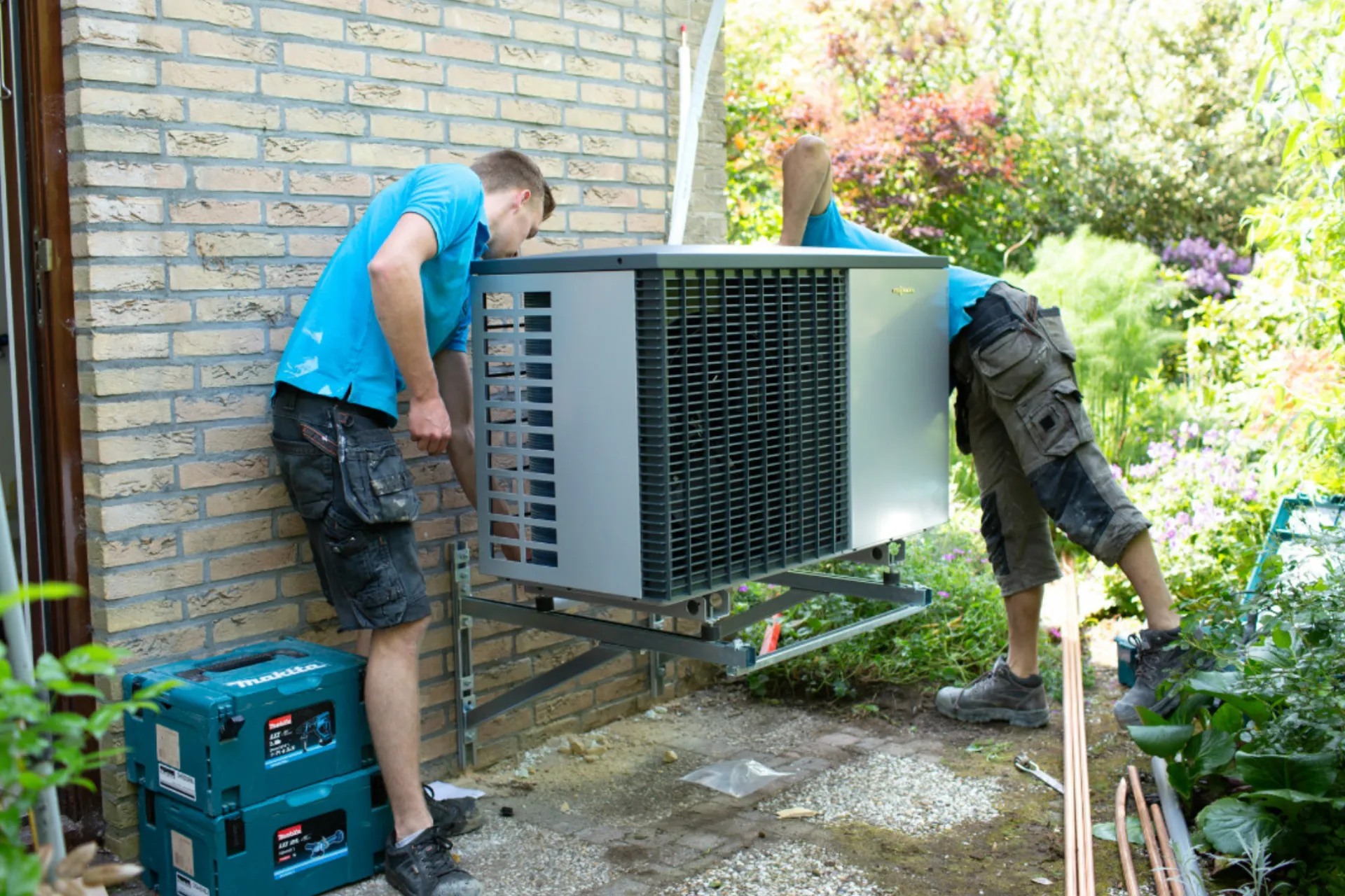 Monteurs plaatsen de buitenunit van een warmtepomp tegen het huis
