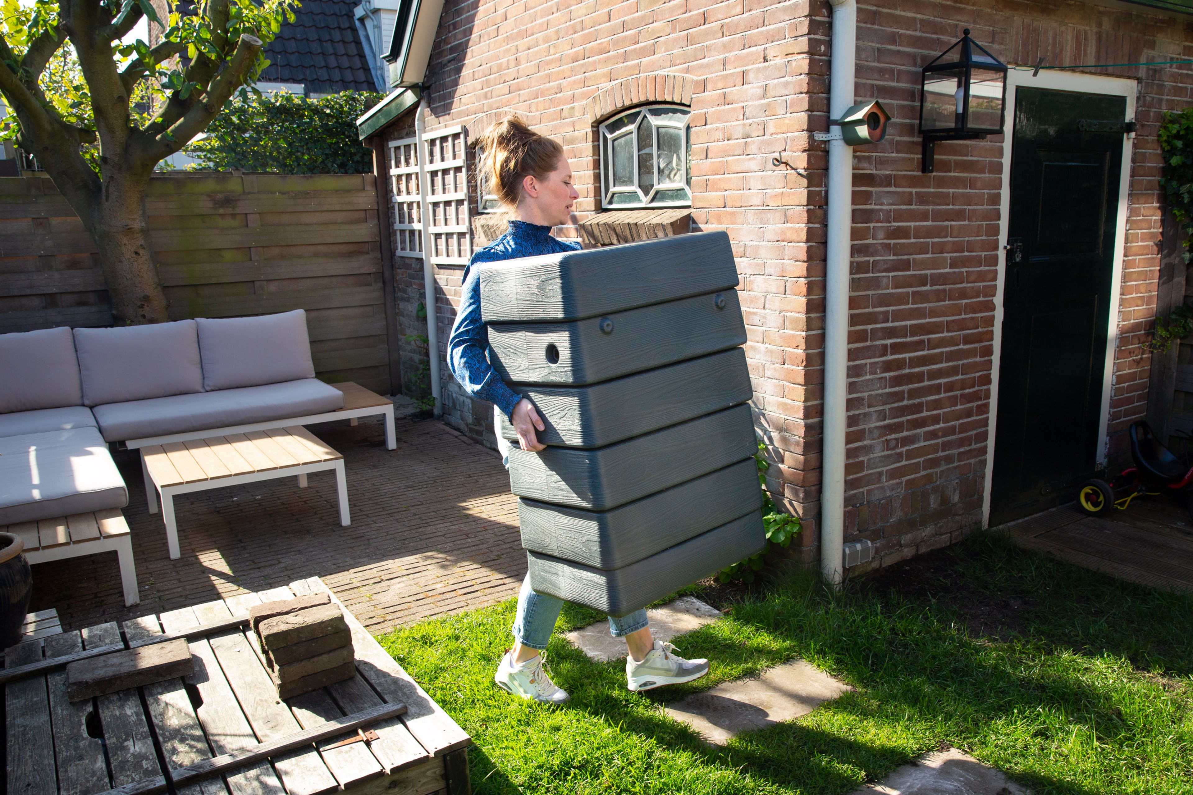 Een vrouw tilt een regenton naar de juiste plek in haar tuin om hem te installeren.