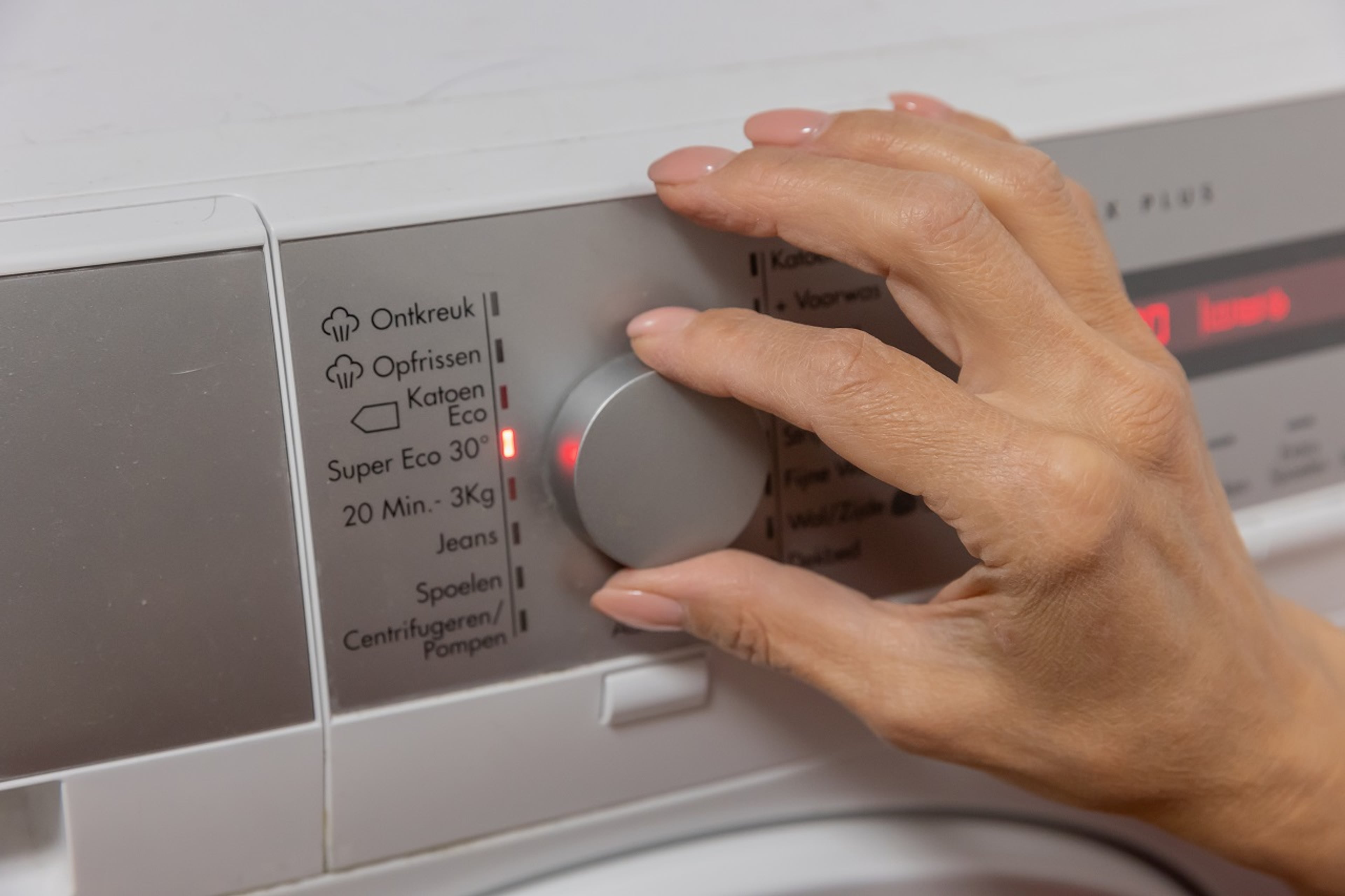 Iemand zet de wasmachine op de ecostand om energie te besparen.