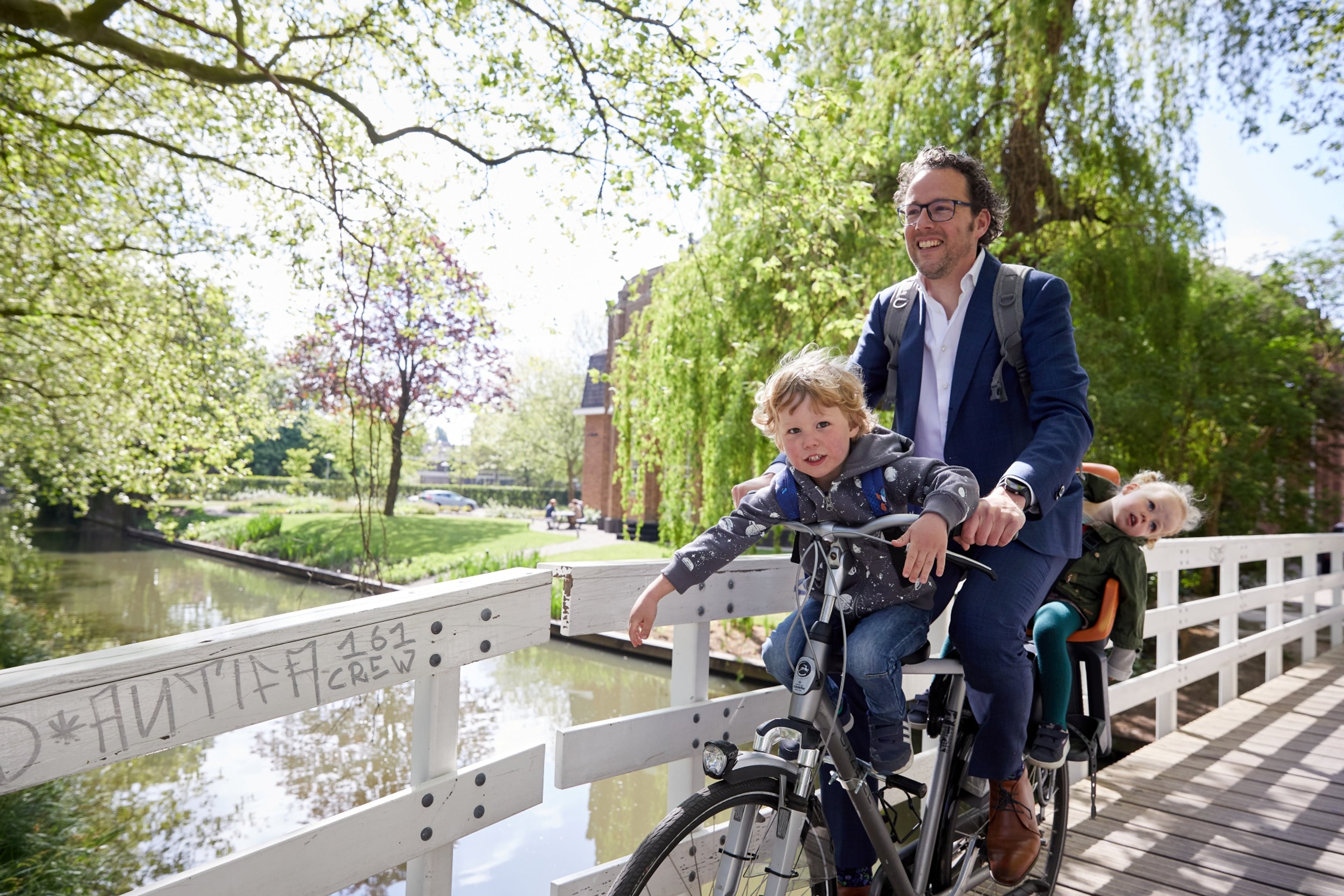 Een man fietst met twee kinderen in kinderzitjes over een brug.