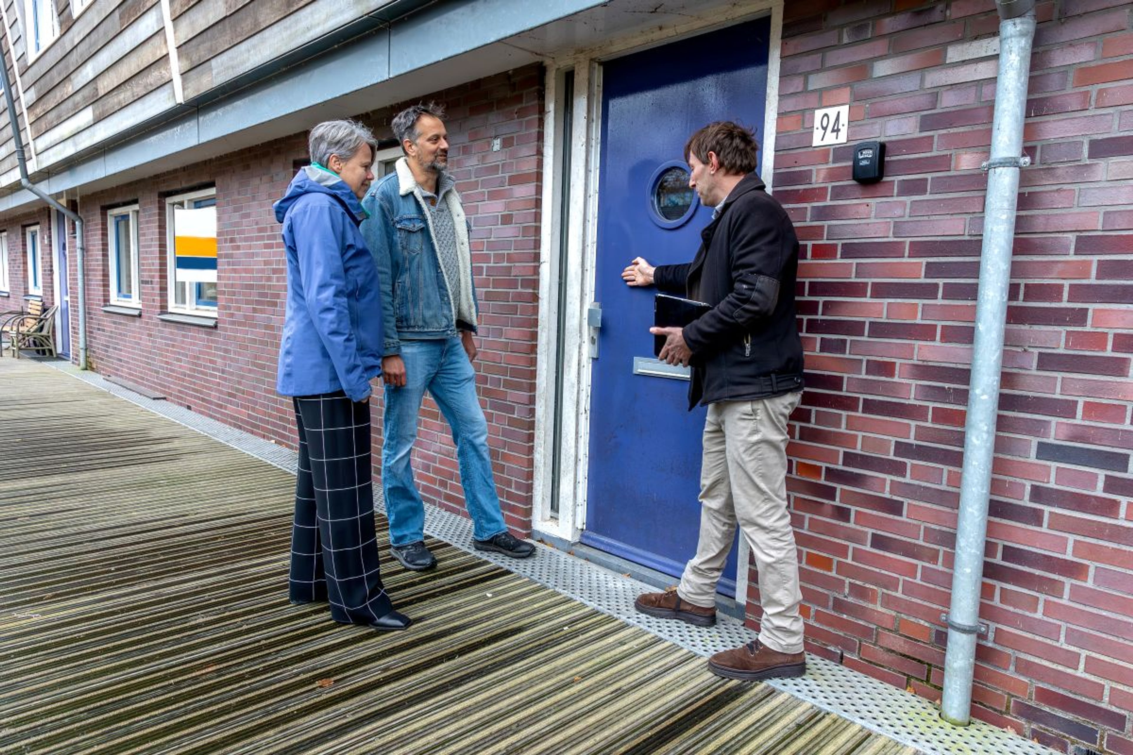 Drie mensen bij een voordeur van een appartement