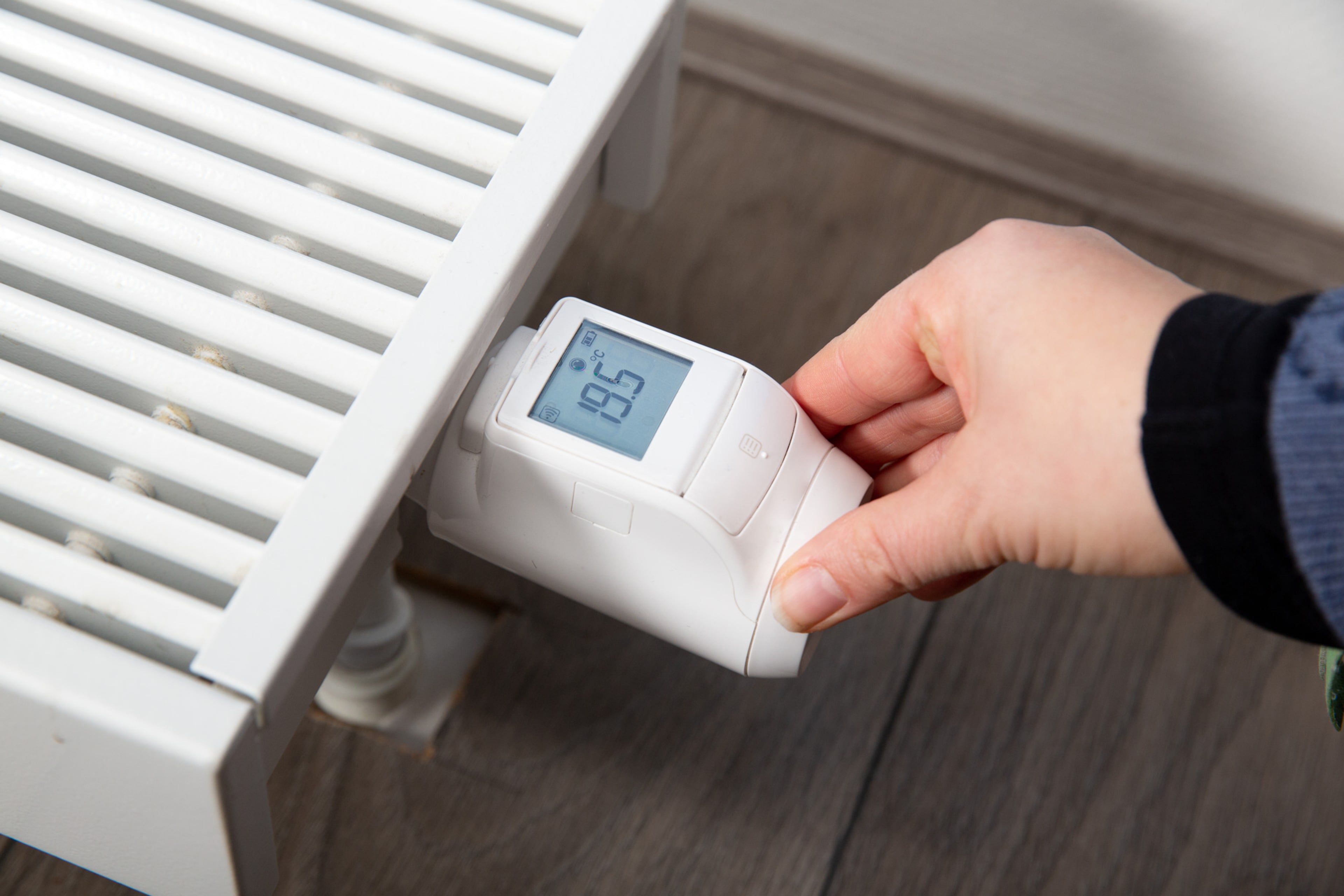 Hand bij digitale thermostaatknop. Goed instellen thermostaat bespaart energie.