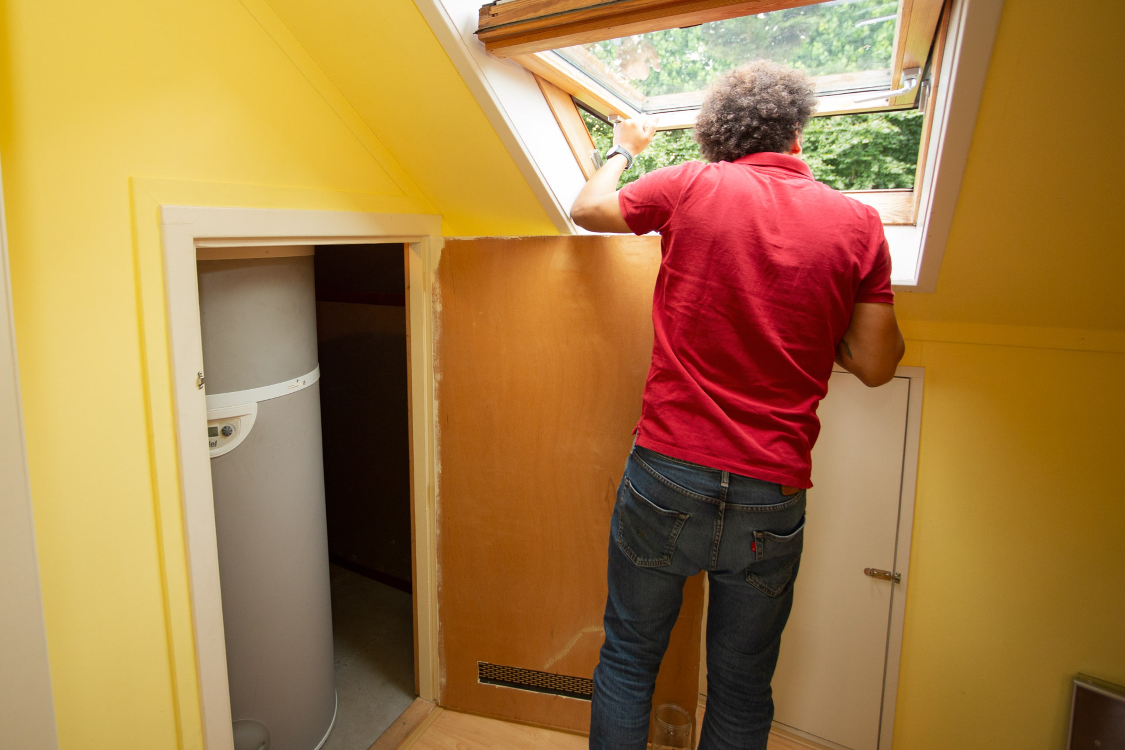 Binnenunit van een volledige warmtepomp, in een kast op zolder. Ernaast kijkt man uit raam.