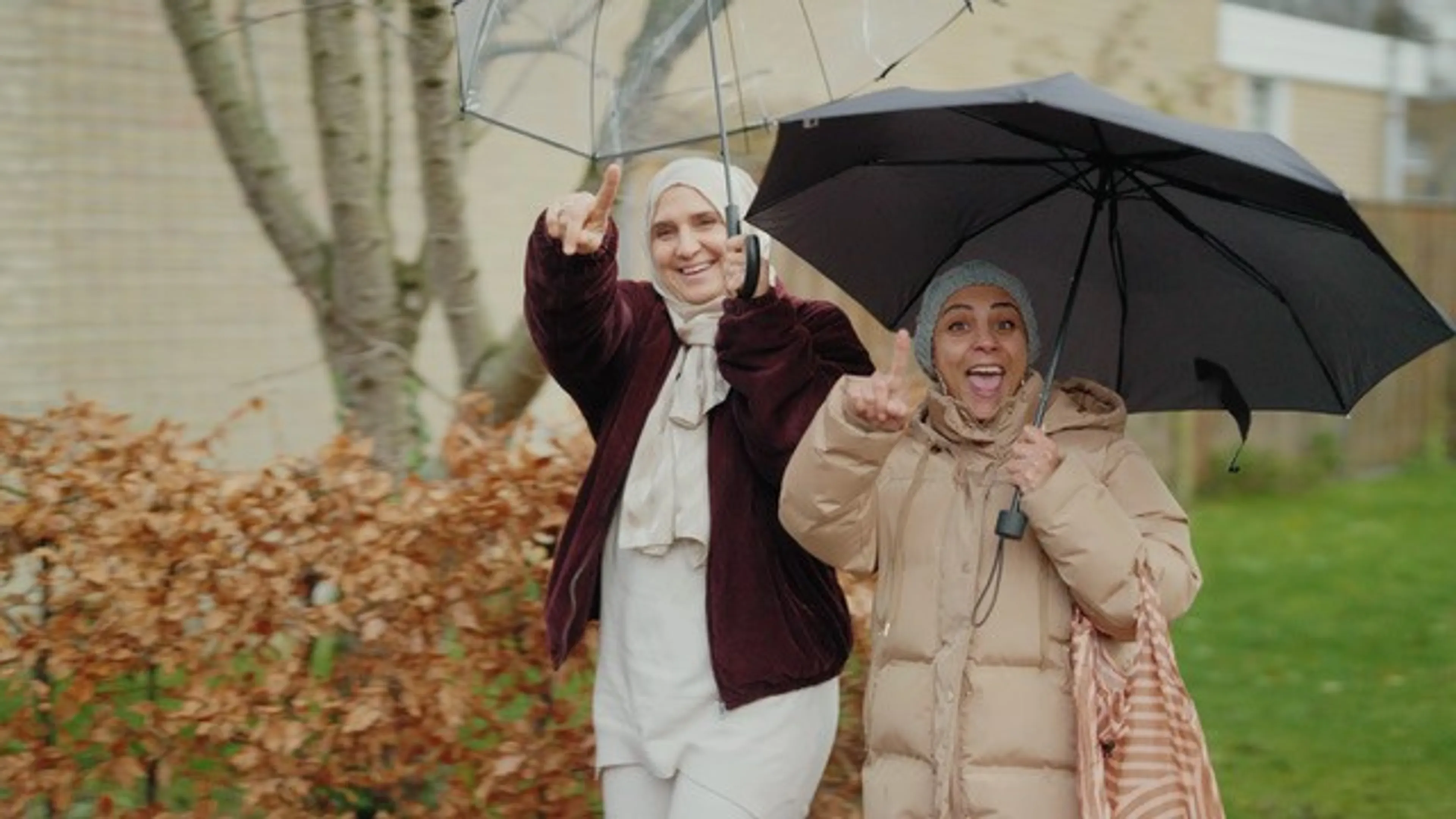 Twee vrouwen onder een paraplu lachen en zwaaien naar de camera