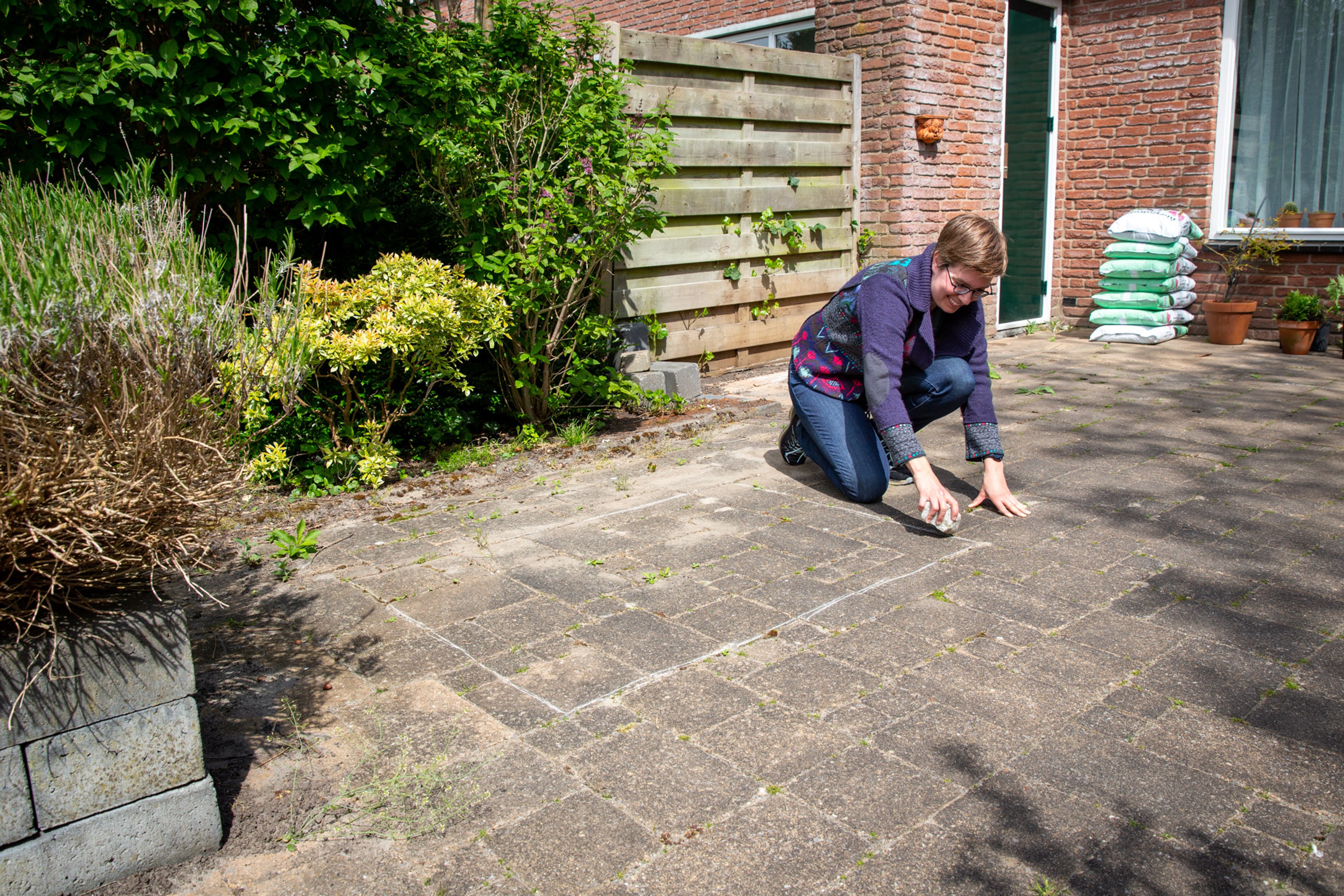 Een vrouw tekent een stuk van haar tegels in de tuin af om ze te vervangen door groen. Door tegels te vervangen door groen, draag je bij aan minder wateroverlast, meer verkoeling en meer biodiversiteit.