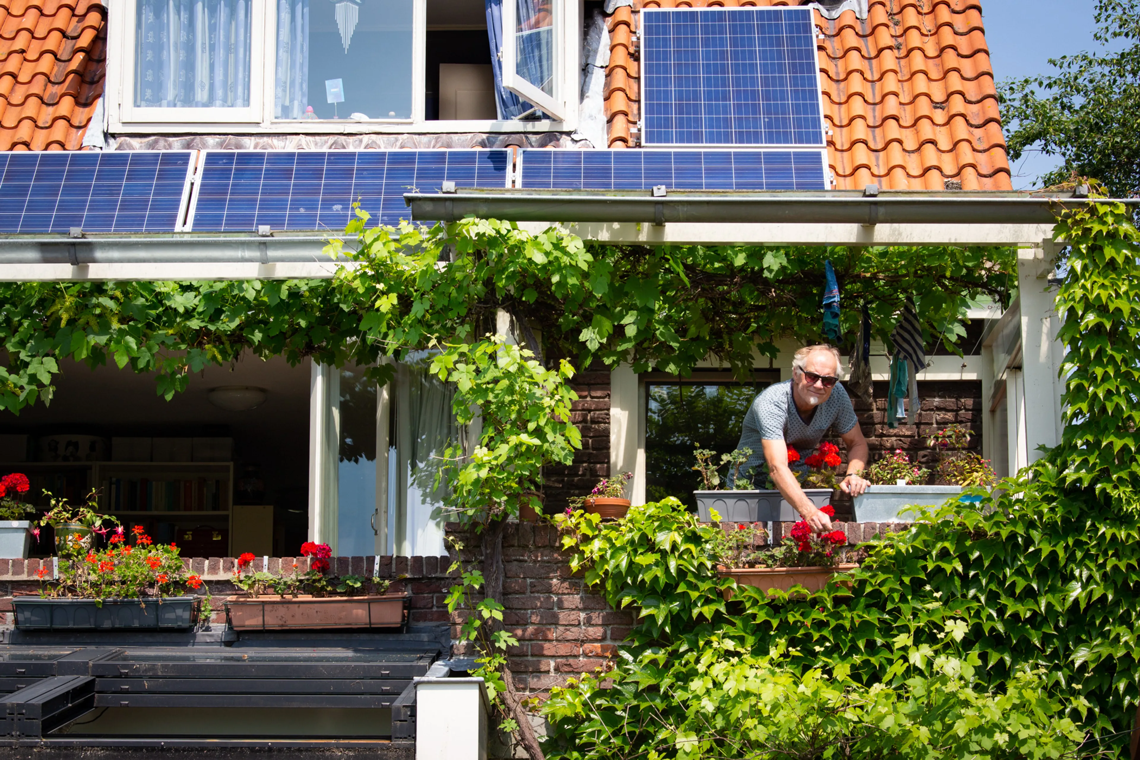 Man verzorgt bloemetjes in de tuin van zijn huurhuis. Zonnepanelen zijn te huren of leasen.