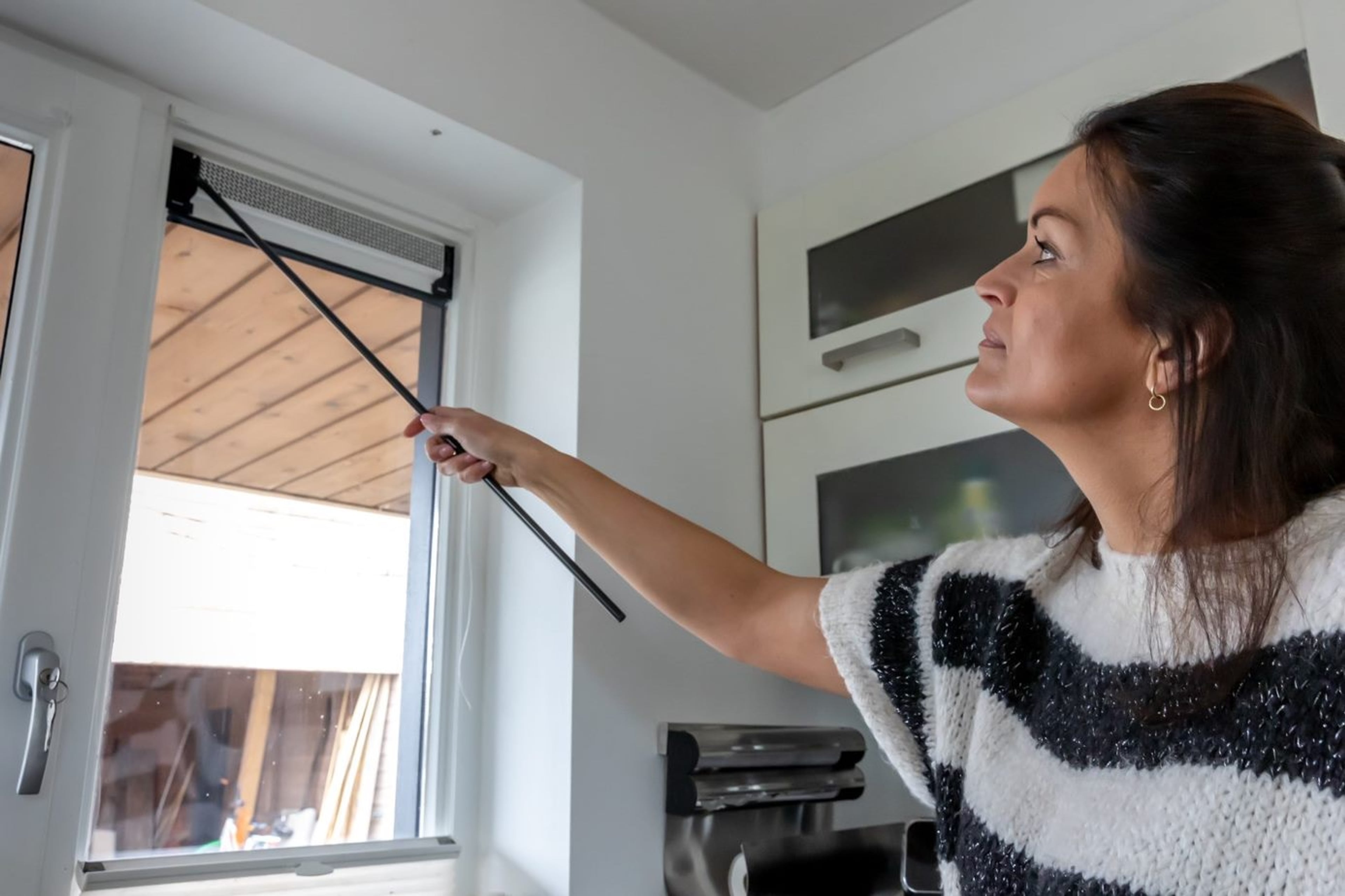 Vrouw zet de ventilatieroosters bij haar raam open.