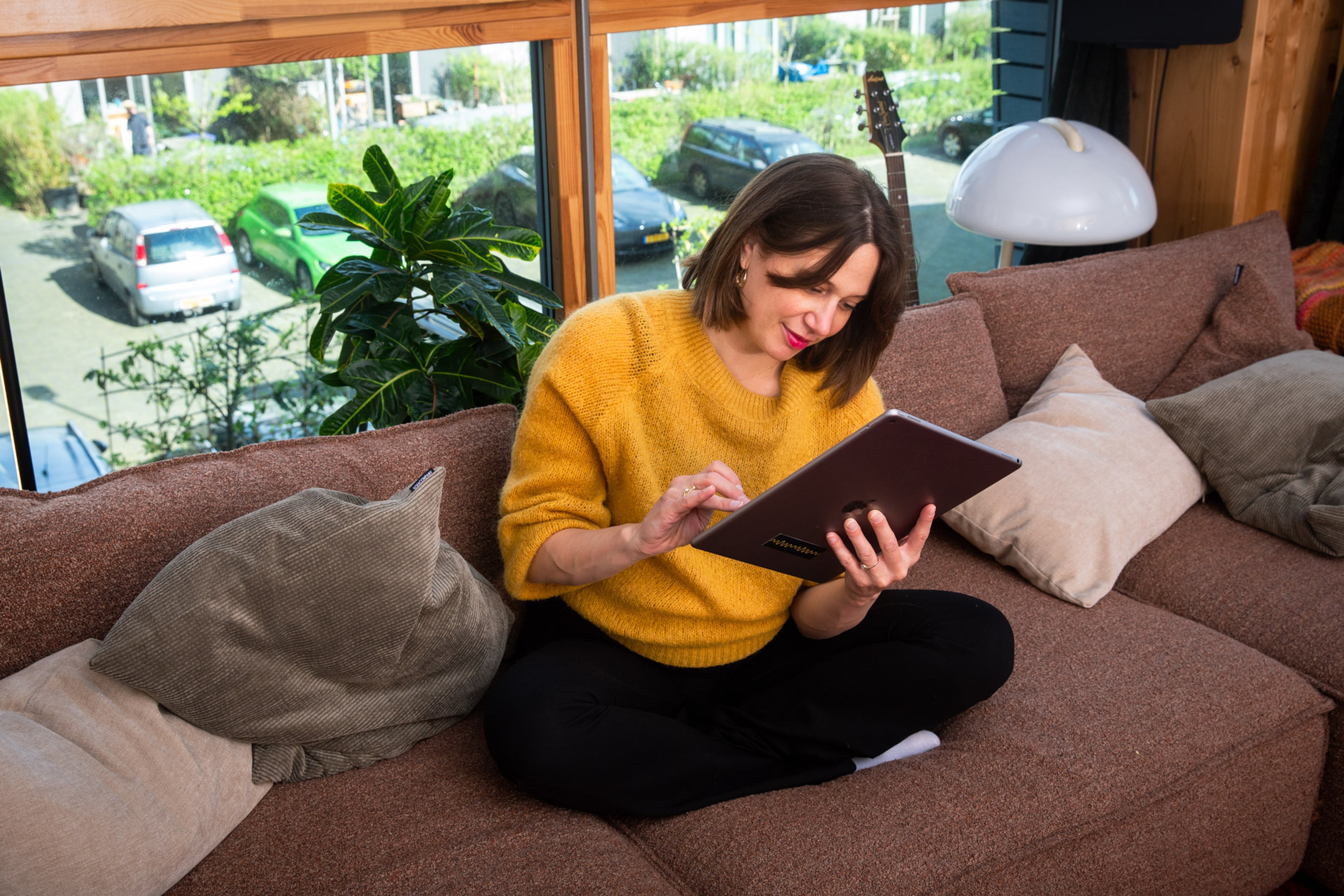 Een vrouw zit met haar tablet op de bank van haar appartement.
