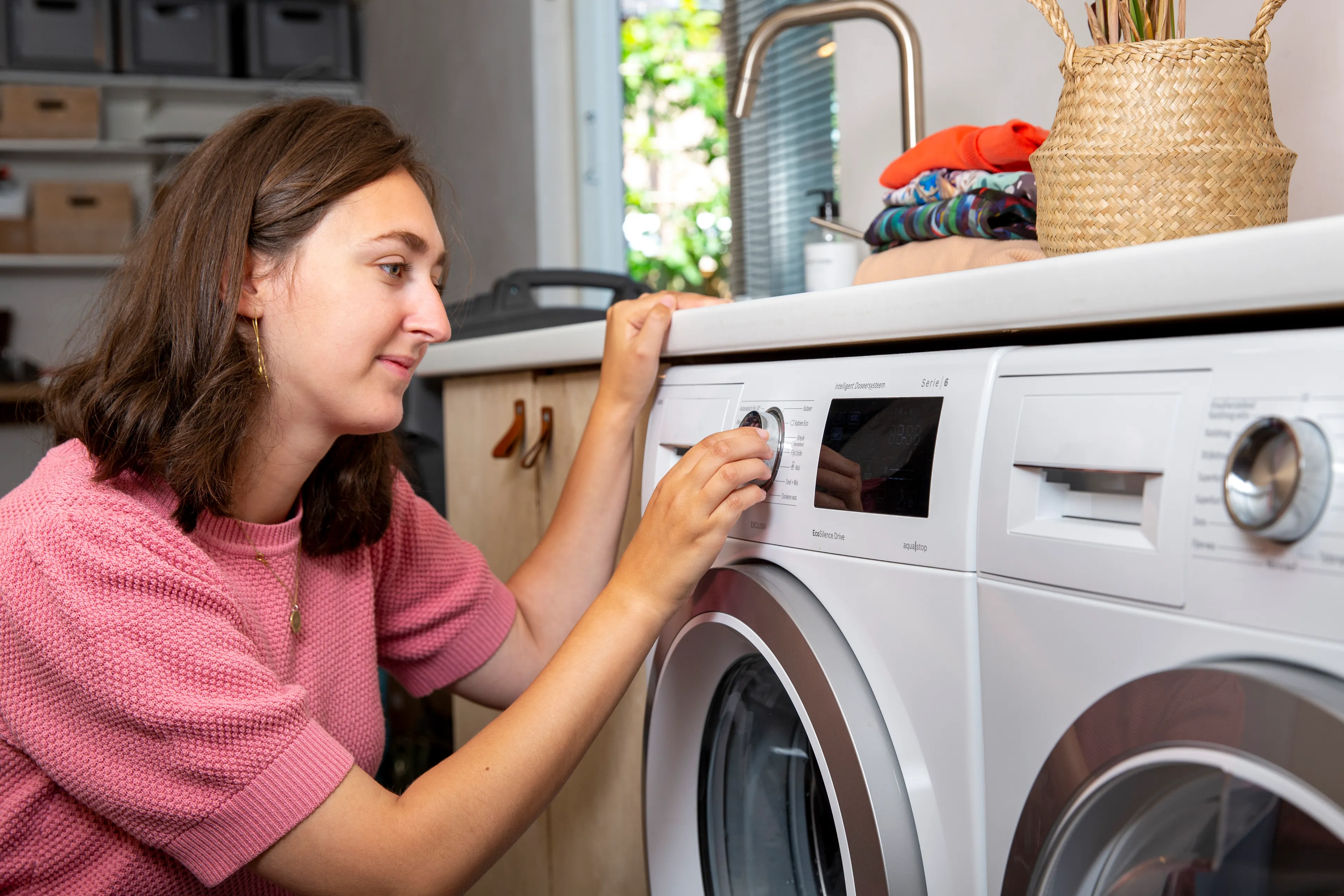 Jonge vrouw bij wasmachine, ze kiest een zuinig programma.