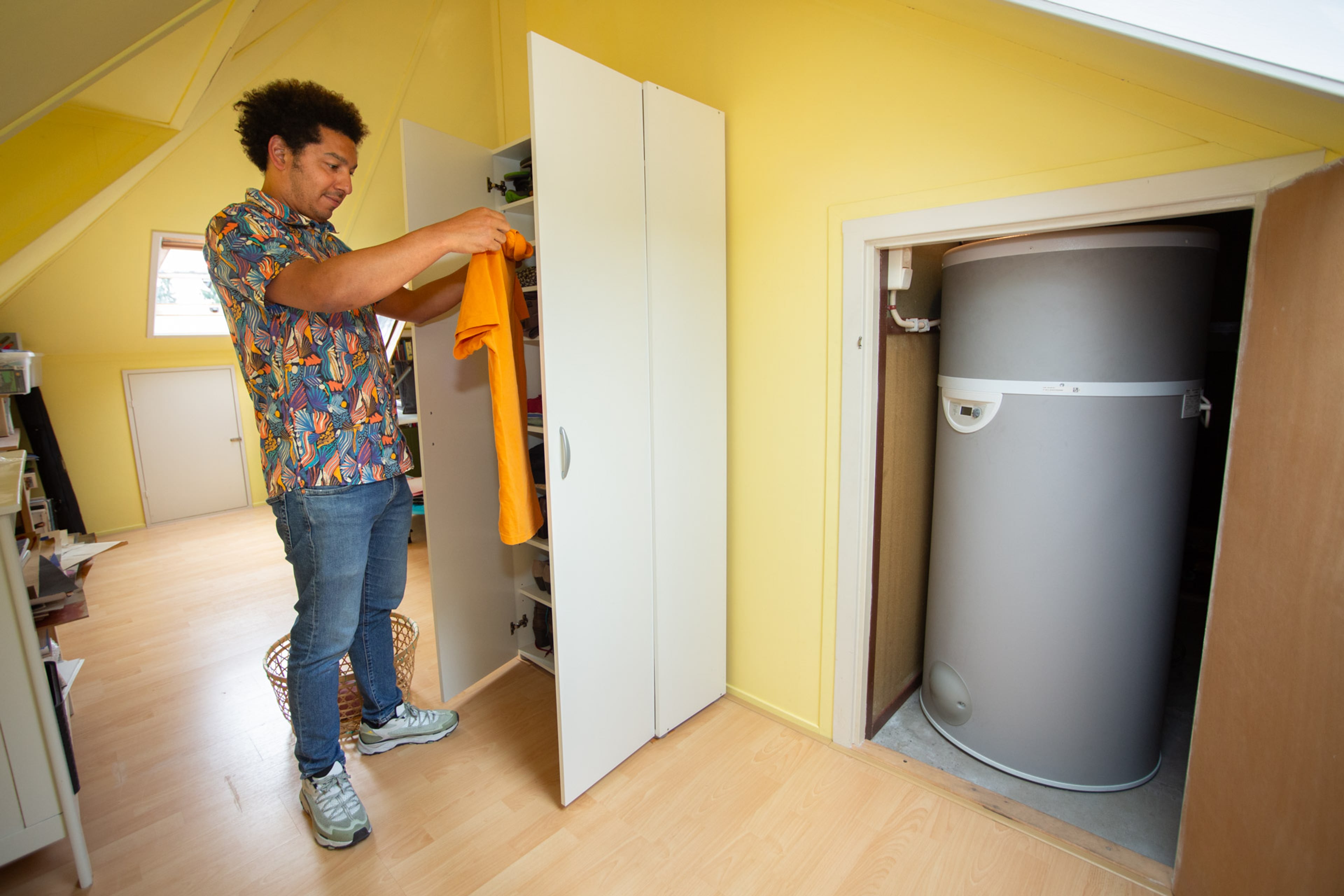 Binnenunit van een volledige warmtepomp, weggewerkt in zolderkast. Ernaast staat een man de was op te vouwen.