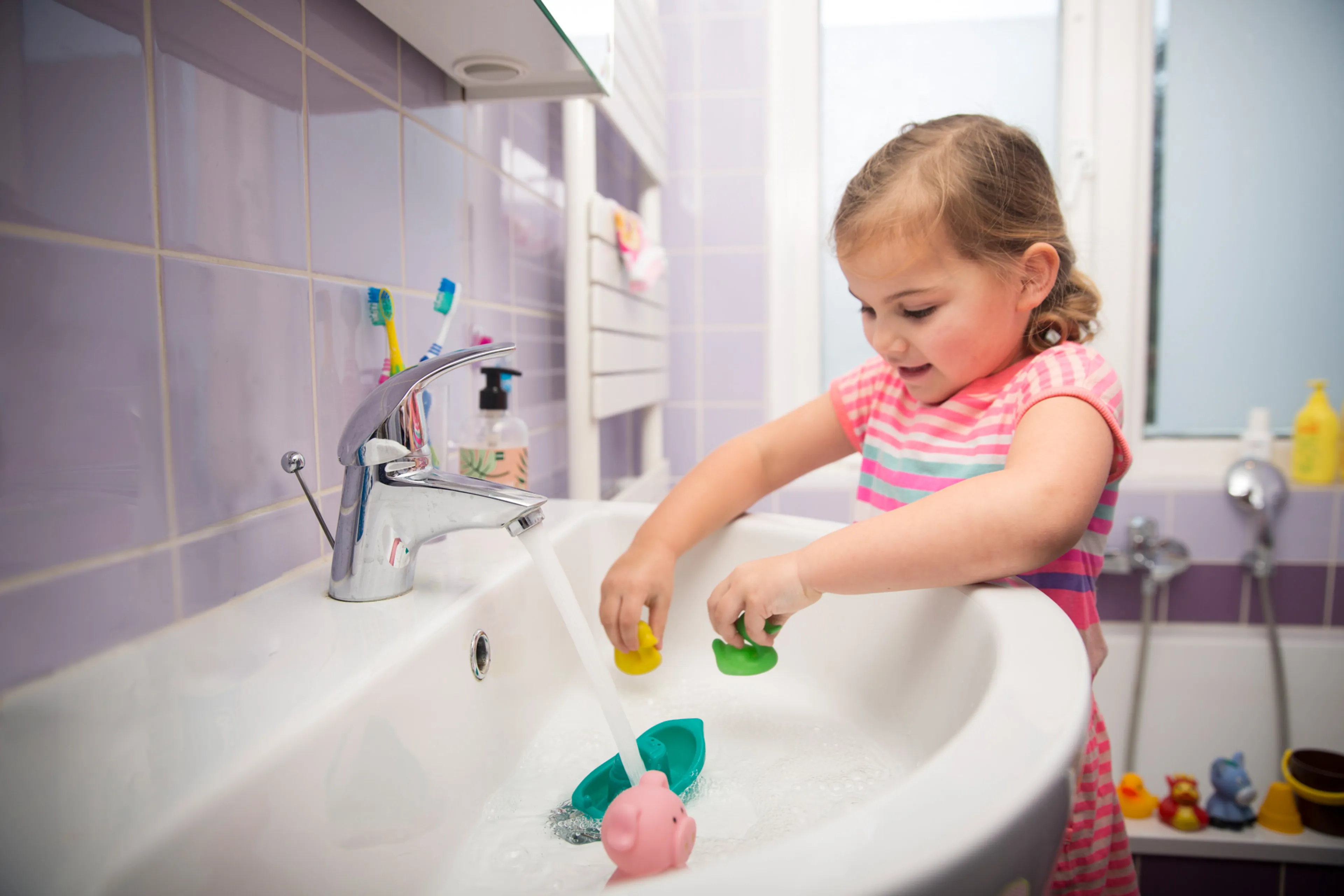 Meisje speelt in wasbak in de badkamer met speelgoed. Verwijder kalk van sanitair.