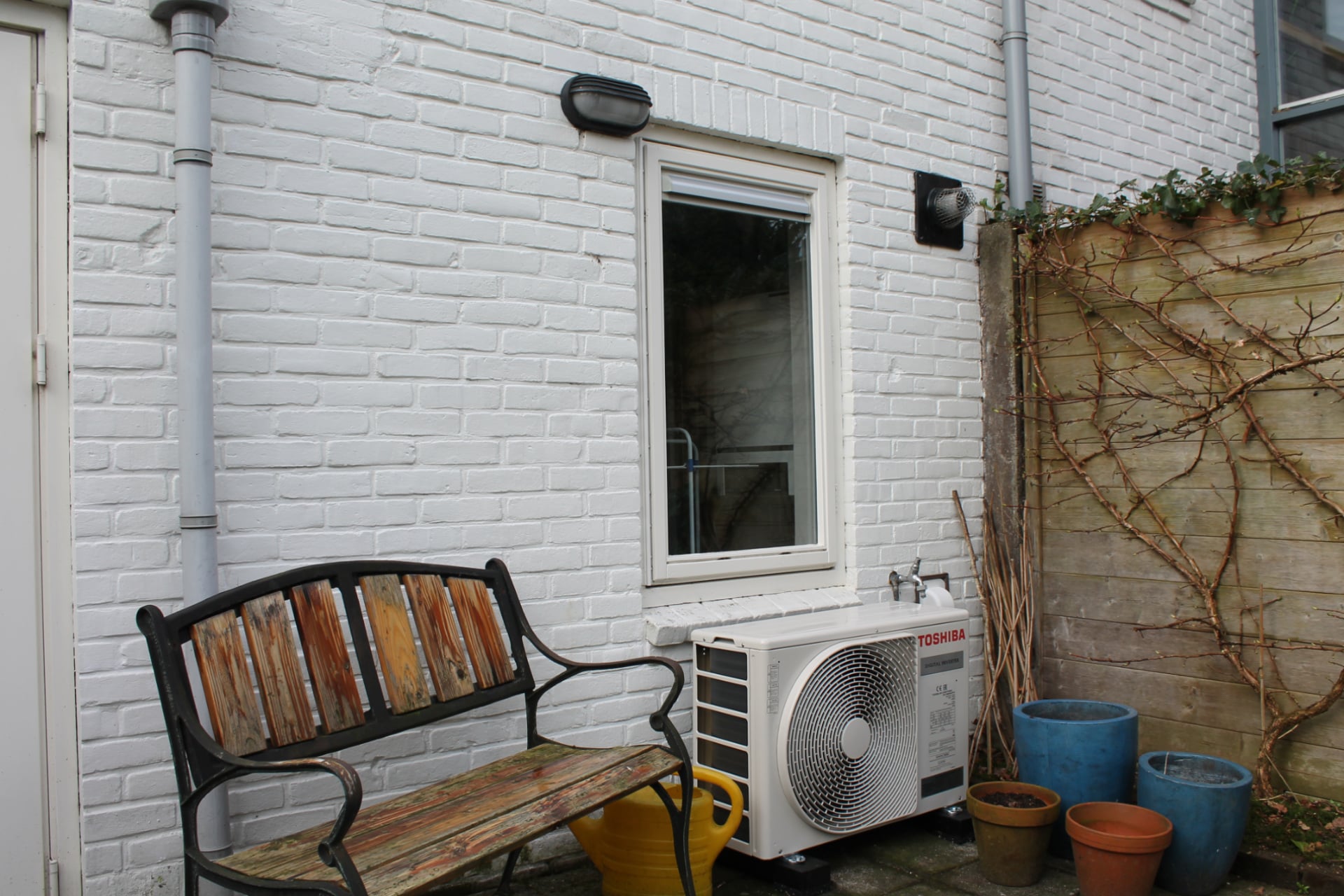 Buitenunit van hybride warmtepomp tegen buitenmuur, onder raam