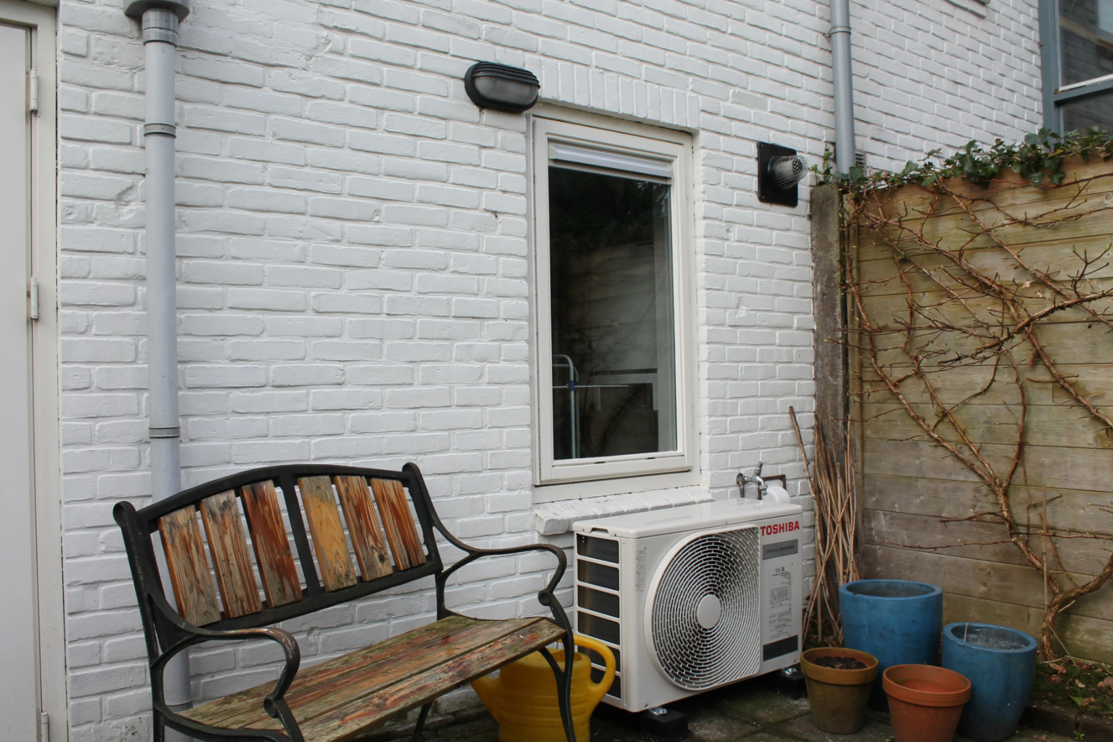 Buitenunit van hybride warmtepomp tegen buitenmuur, onder raam