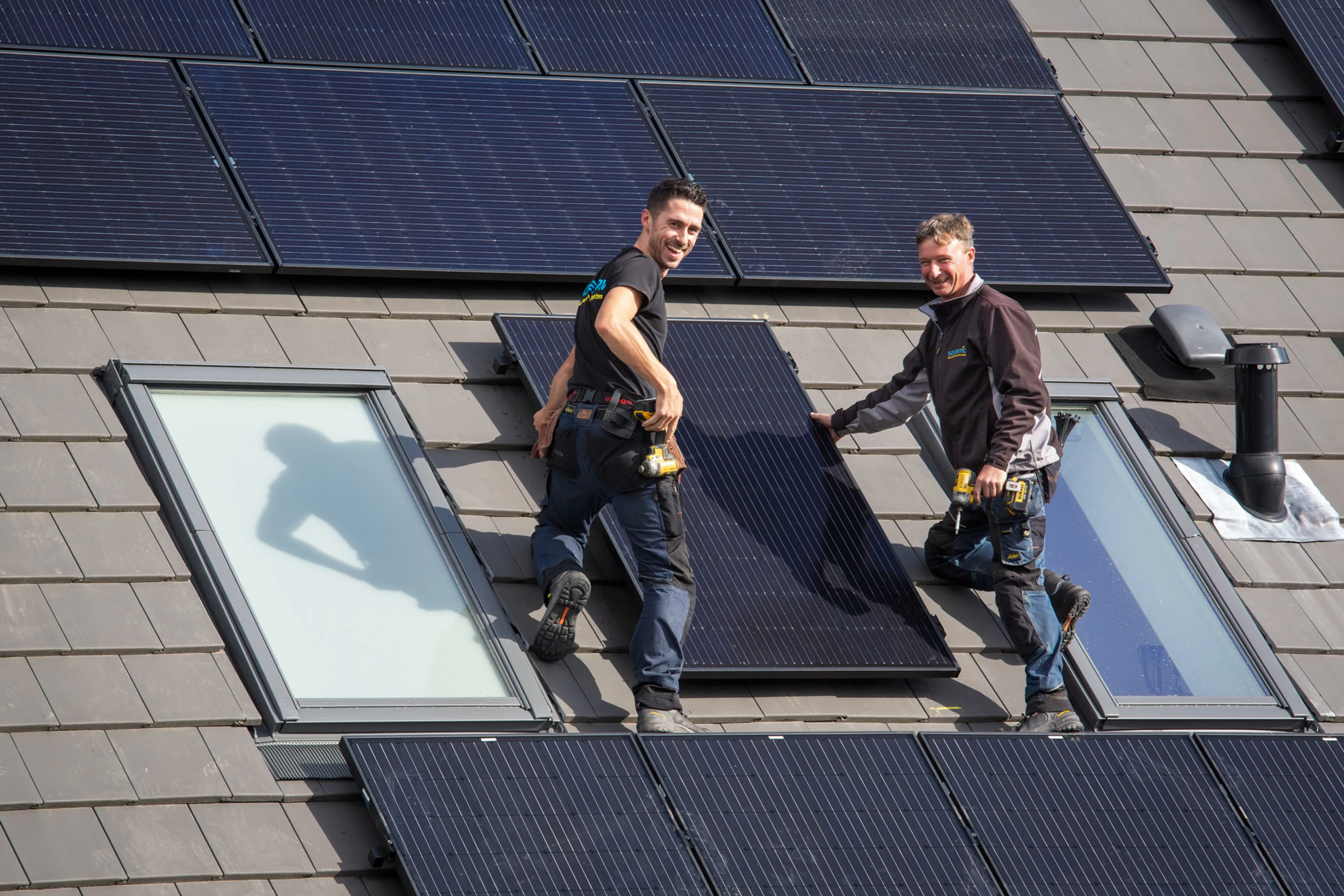 Twee mannen installeren zonnepanelen op dak en poseren voor foto.
