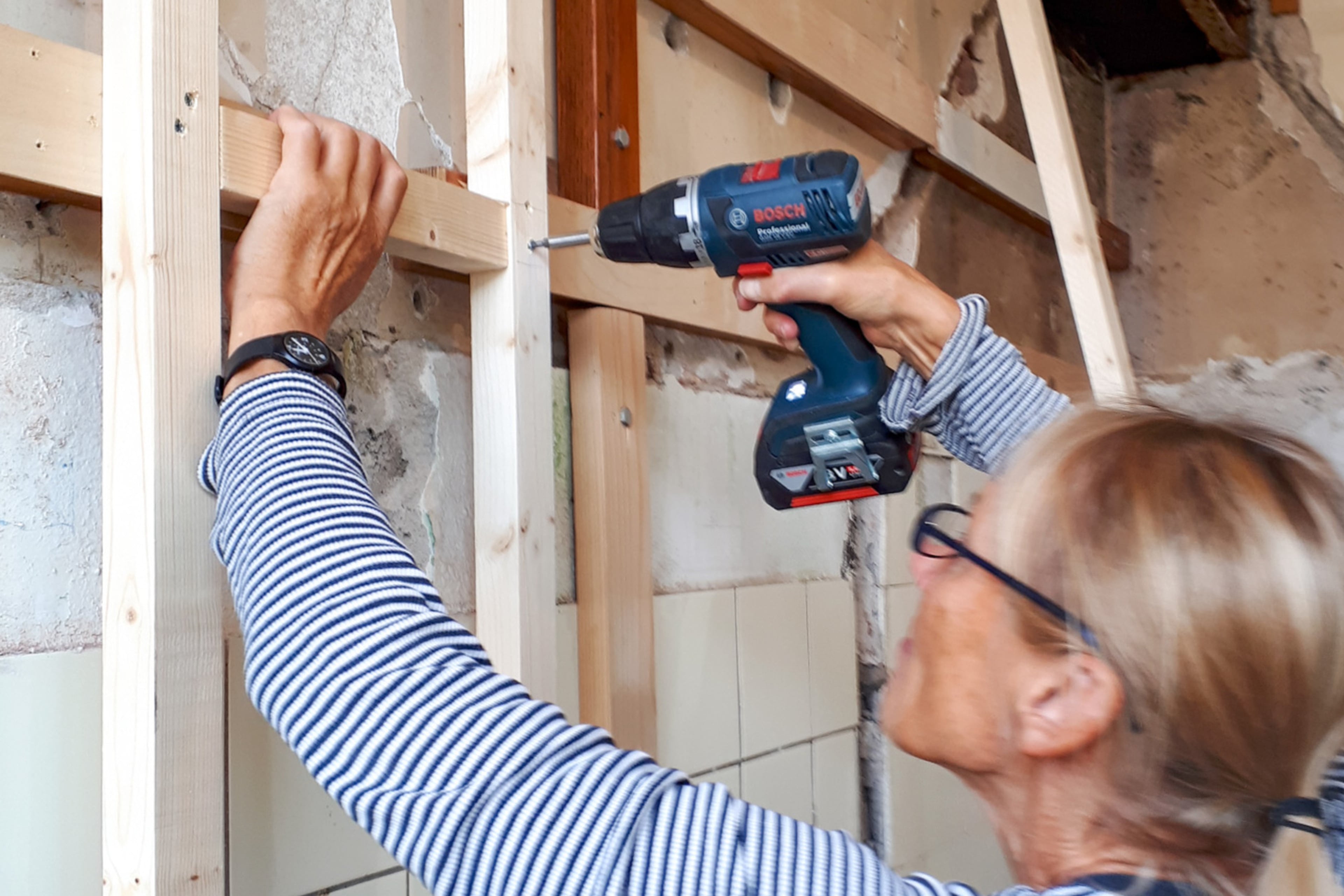 Vrouw boort gevelisolatie aan de binnenkant van de muur. Voorzetwand plaatsen.