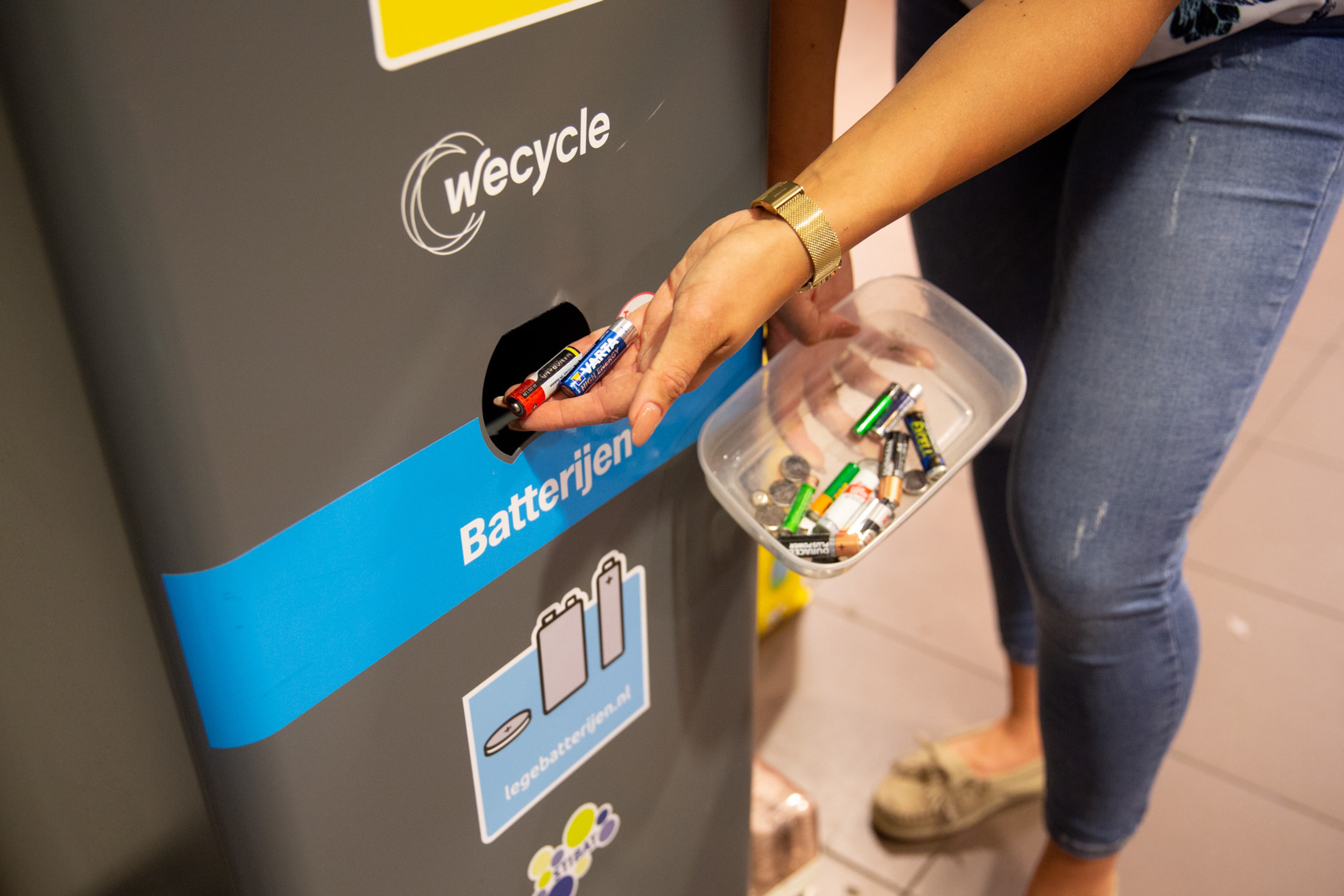 Vrouw levert batterijen in, in een wecycle inzamelbak. Lege batterijen en accu's inleveren spaart veel nieuwe grondstoffen uit.