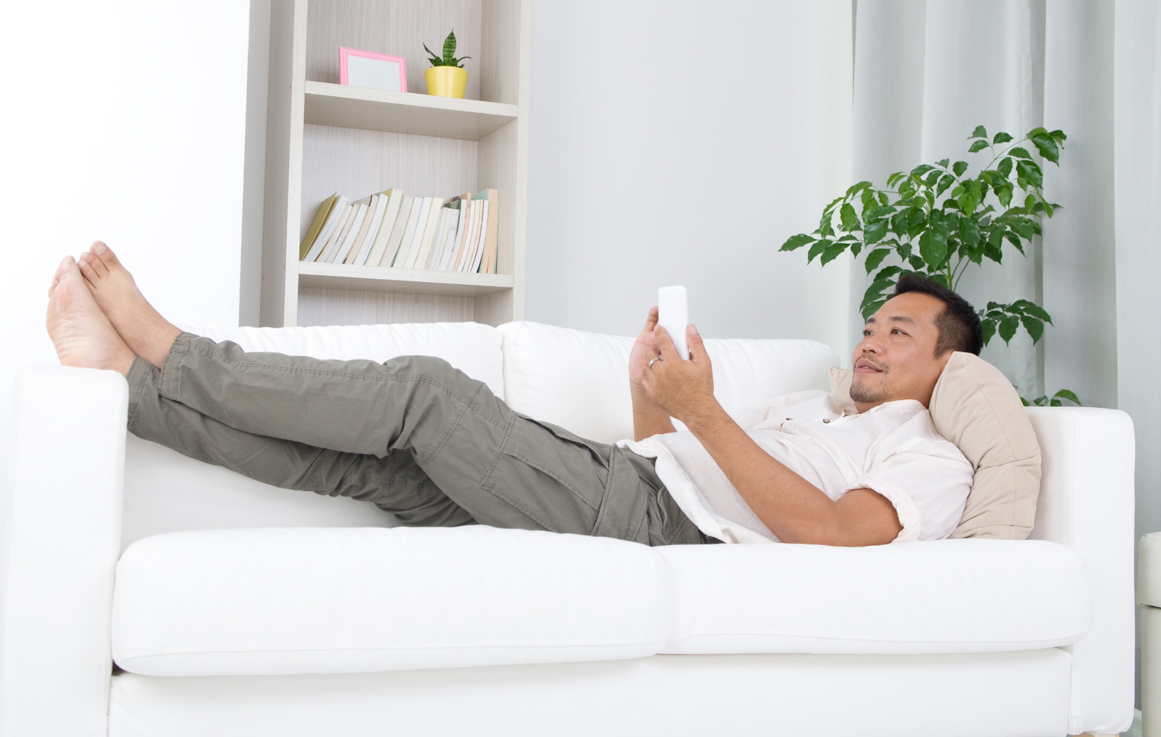 Man liggend op bank met telefoon in de handen. Je huis energiezuinig verwarmen met een slimme thermostaat.