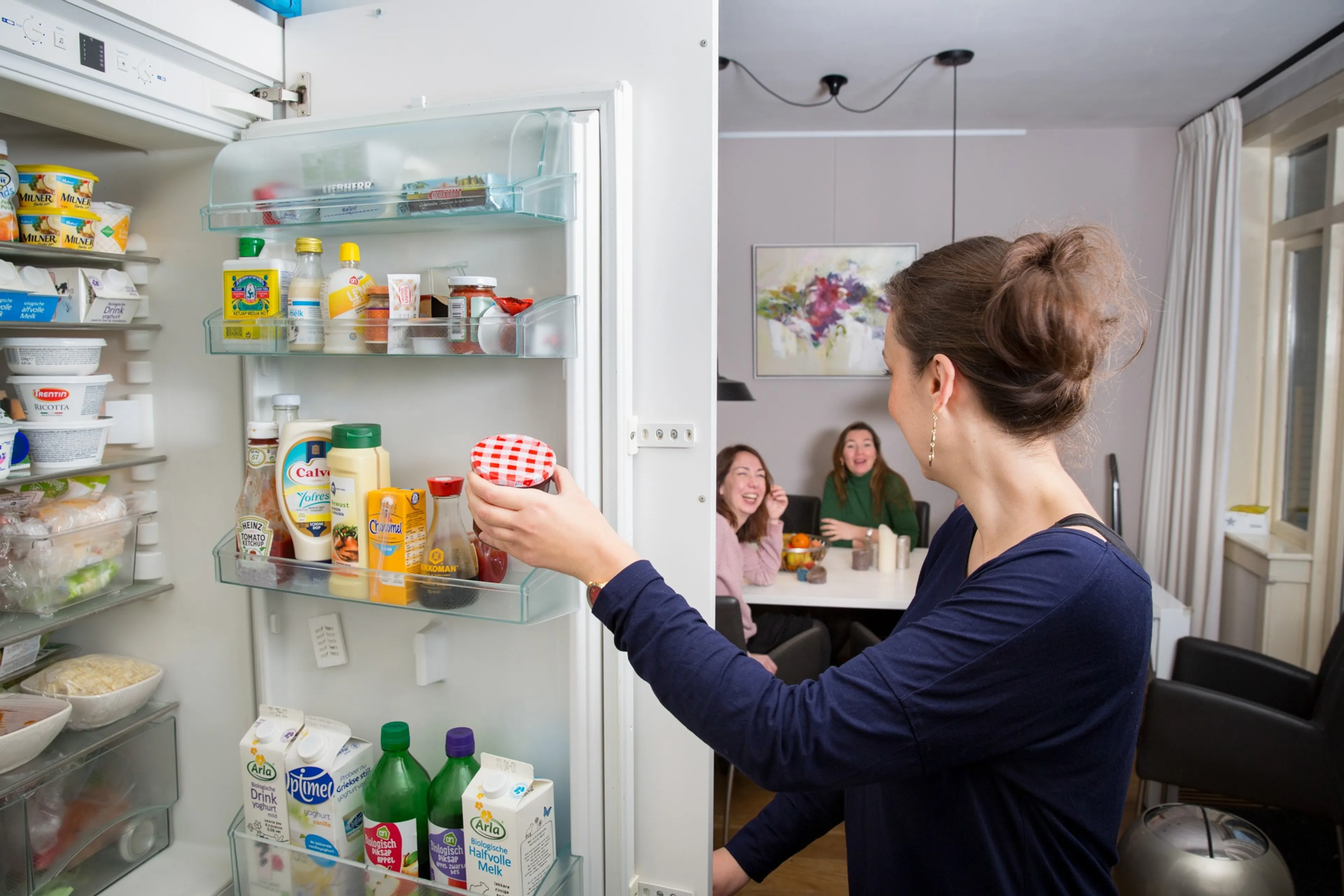 Vrouw pakt jam uit de koelkast. Let op het stroomverbruik van koelkasten en vriezers.