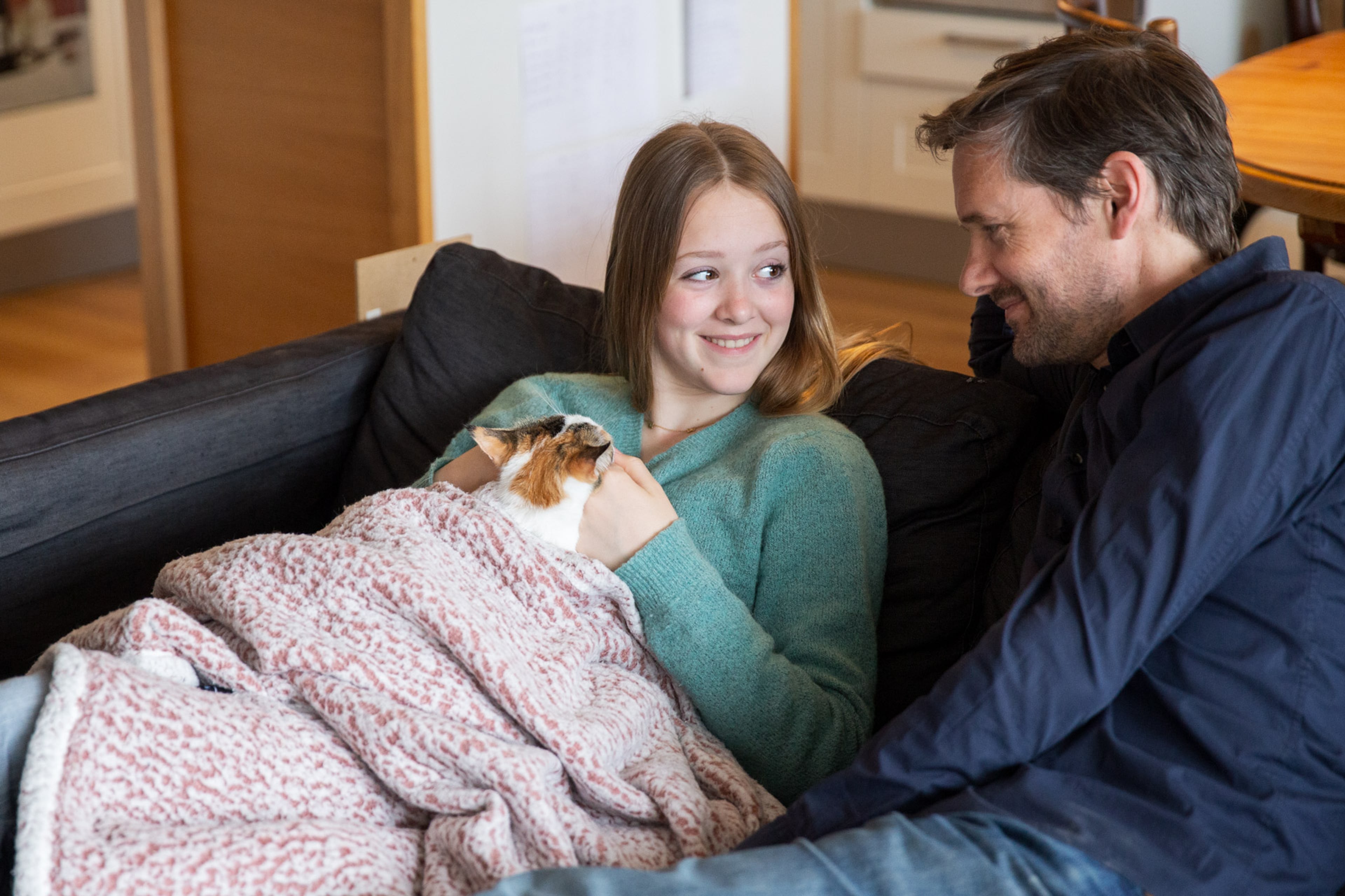 Meisje onder dekentje op de bank, kat op schoot.