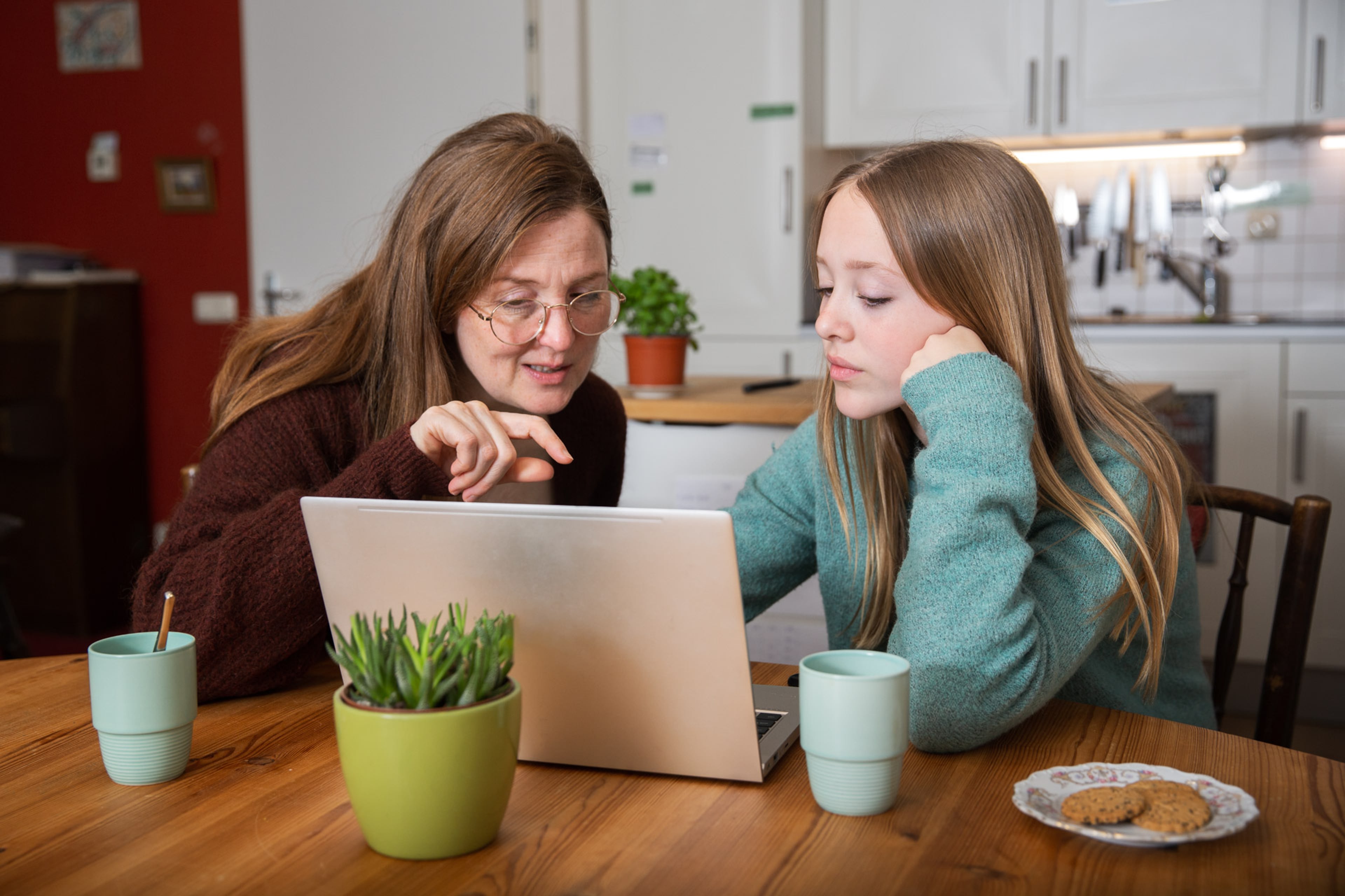Foto van een vrouw en een meisje achter een laptop. De vrouw wijst naar iets op het scherm.