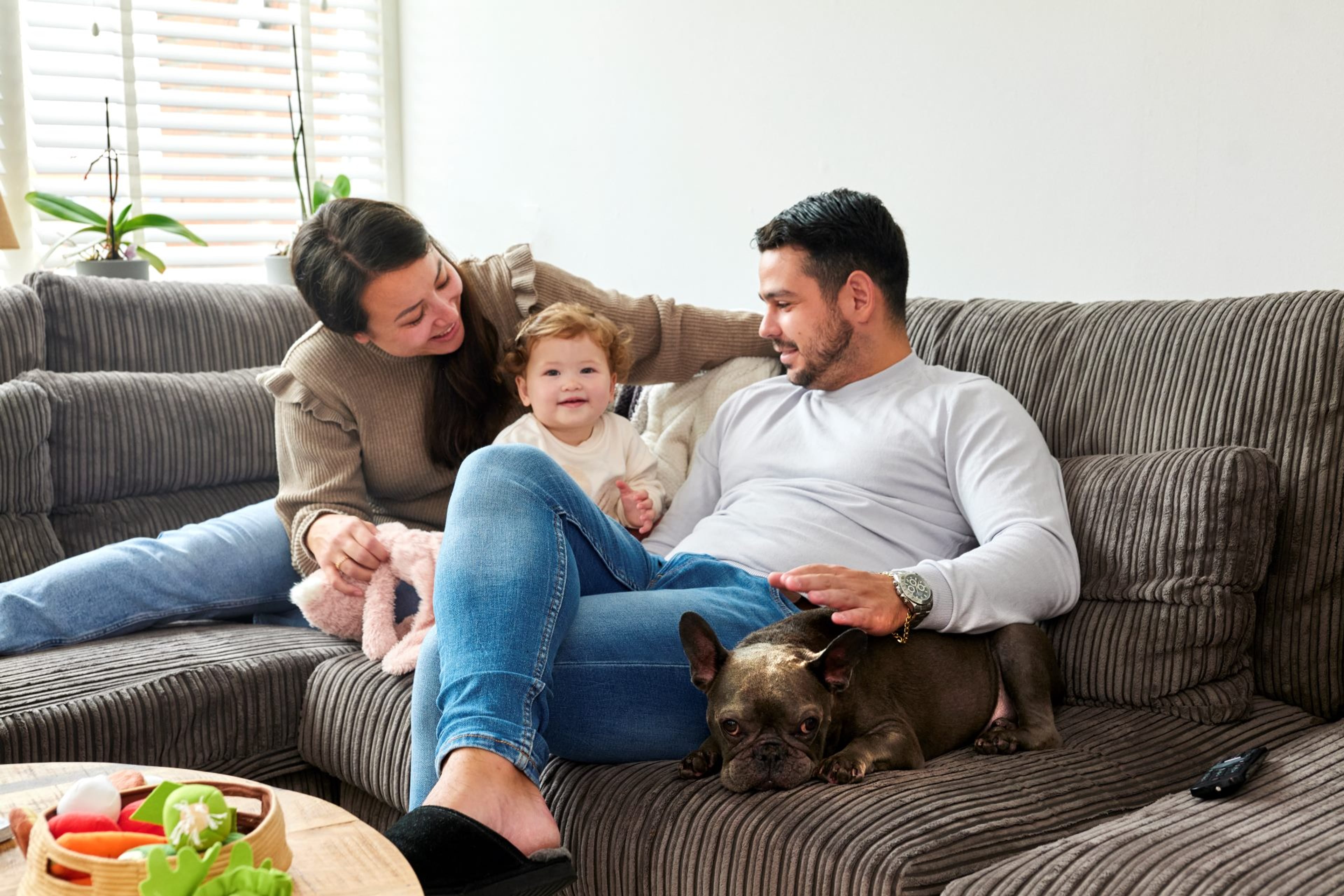 Een vrouw, een peuter, een man en een hond zitten samen op de bank.