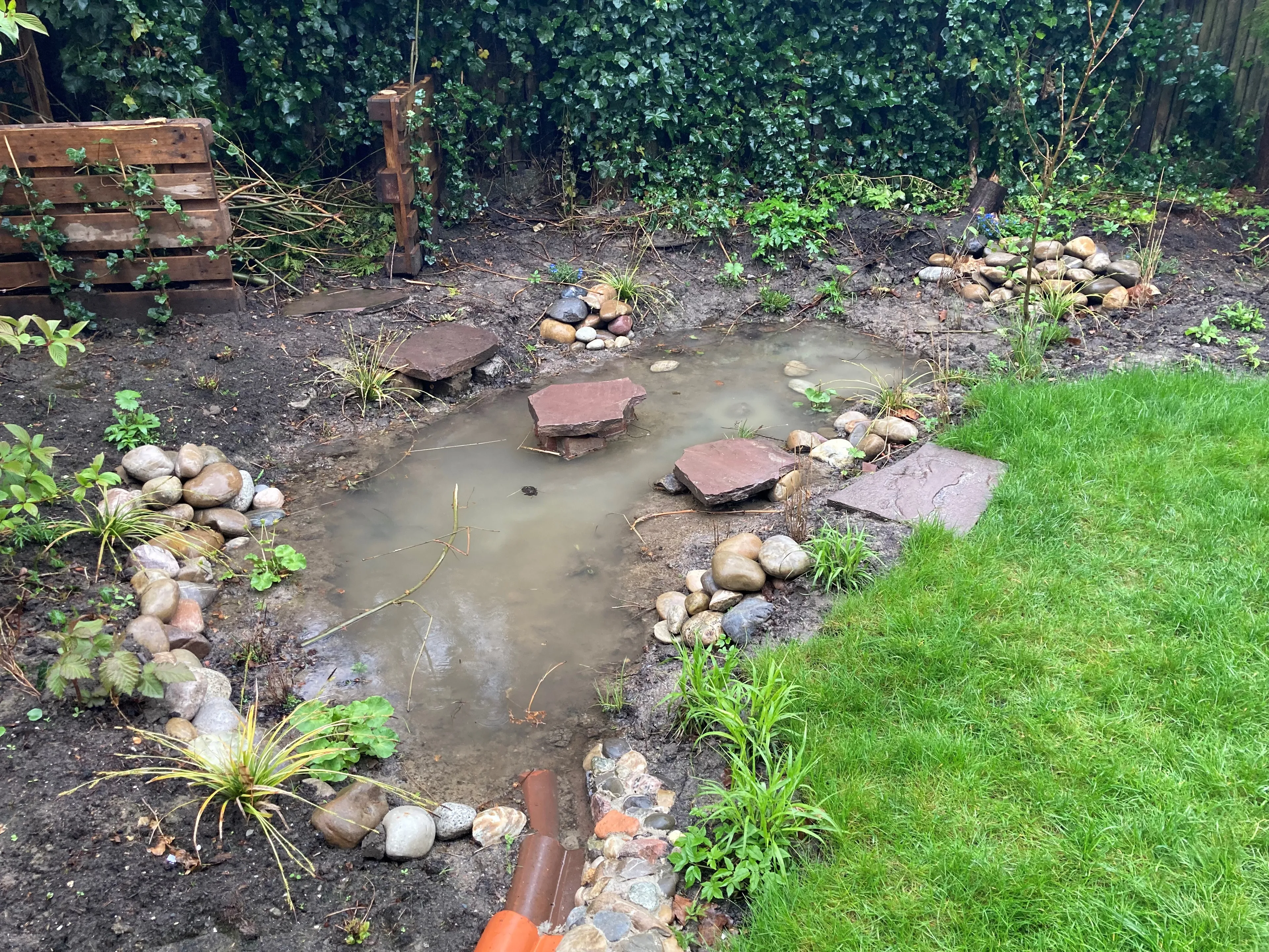 Foto van een met regenwater gevulde wadi met stapstenen. Een wadi kan helpen met de opvang van regenwater.