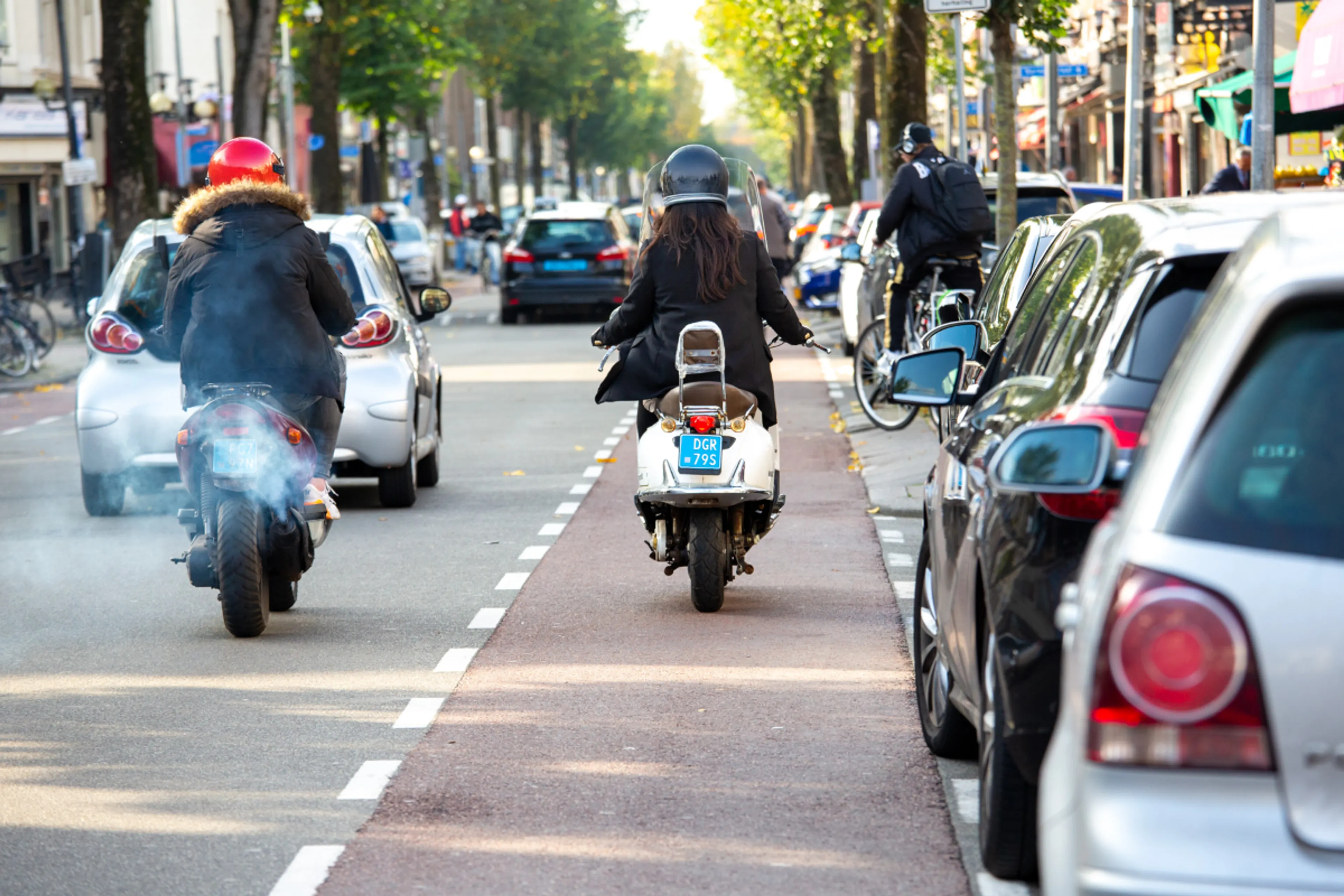 Een benzinescooter en elektrische scooter rijden naast elkaar. De elektrische scooter heeft geen uitstoot van giftige stoffen.