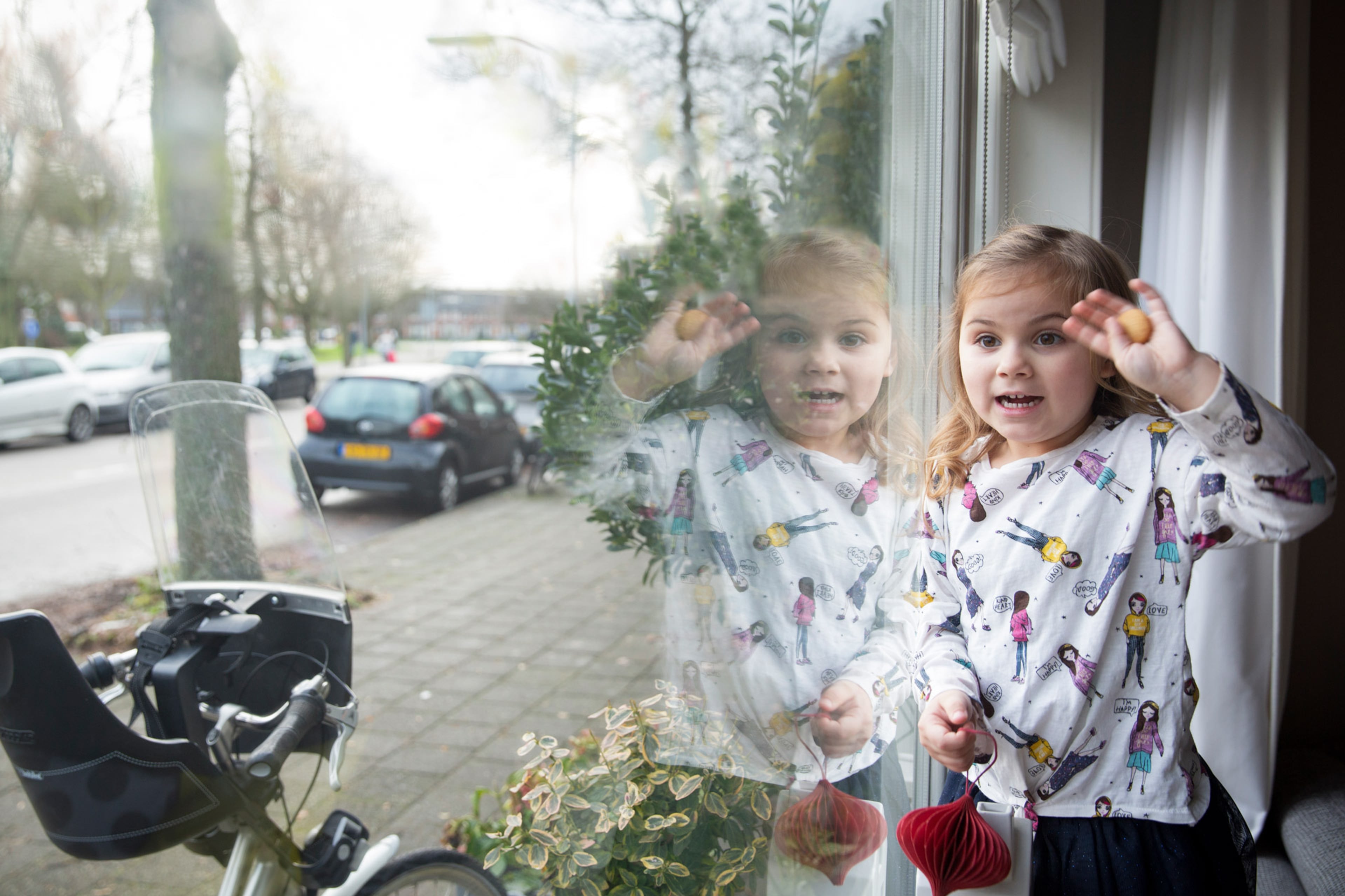 Meisje staat bij het raam en zwaait. Met isolatieglas is het lekker warm in huis en bespaar je energie.