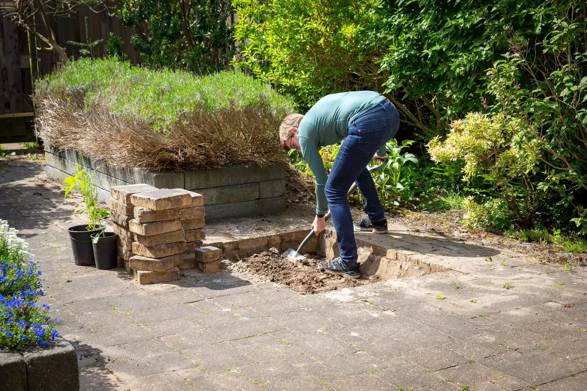 Een vrouw heeft tegels uit haar tuin gehaald en schept de zandgrond weg, zodat er tuinaarde in kan. Door tegels te vervangen door groen, draag je bij aan minder wateroverlast, meer verkoeling en meer biodiversiteit.