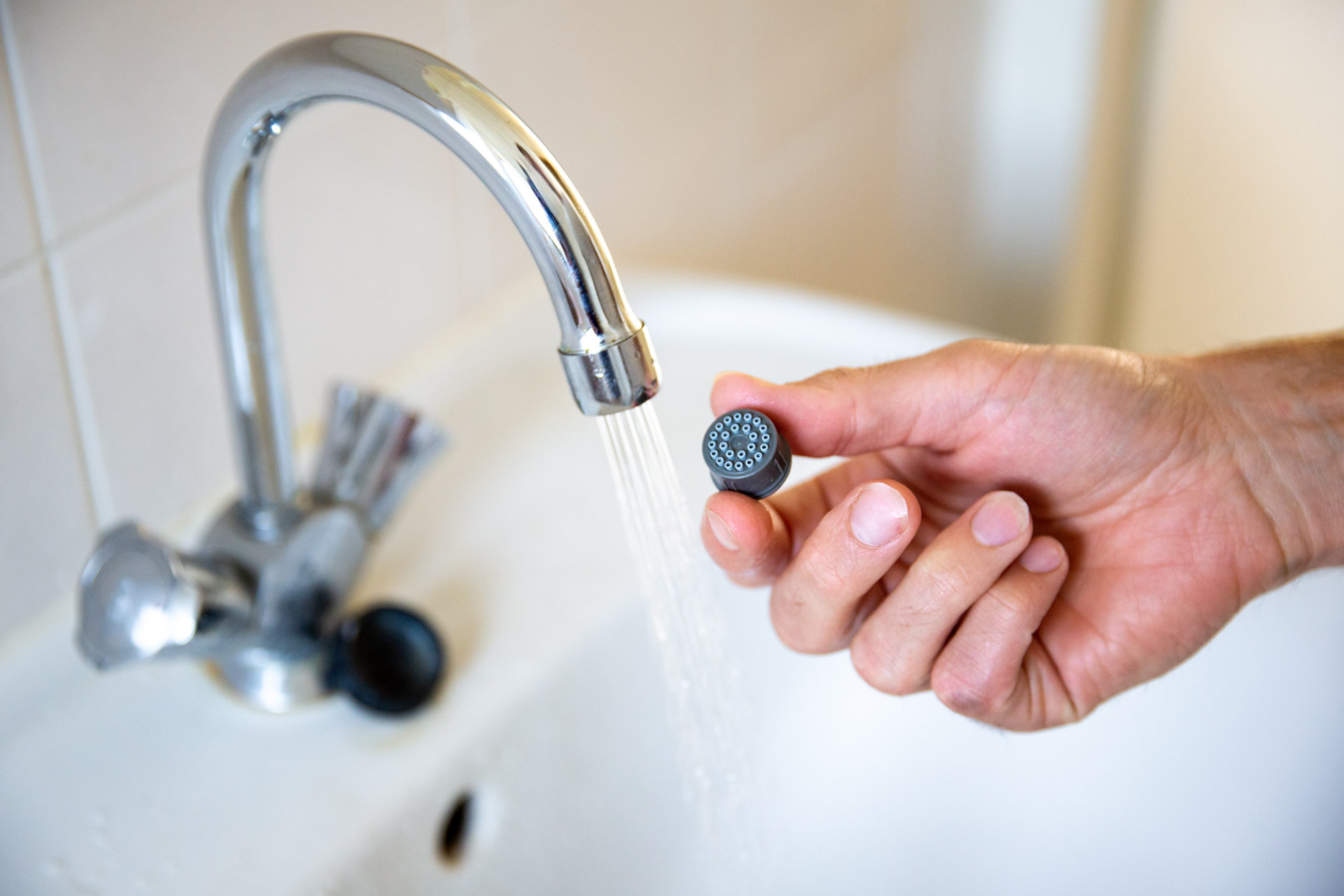 Hand die waterbesparend mondstuk in de kraan zet.