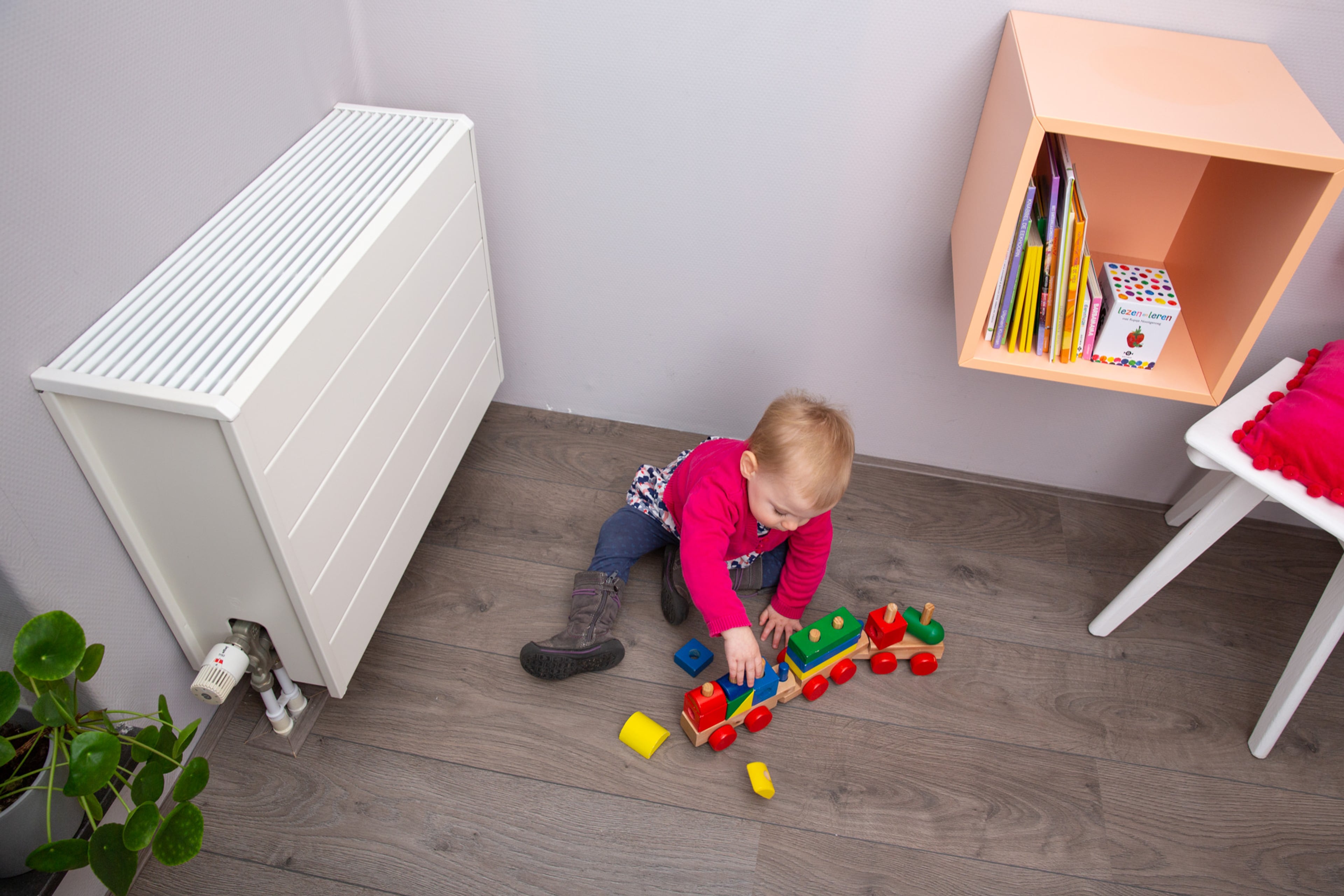 Kind speelt met speelgoedtrein naast radiator.