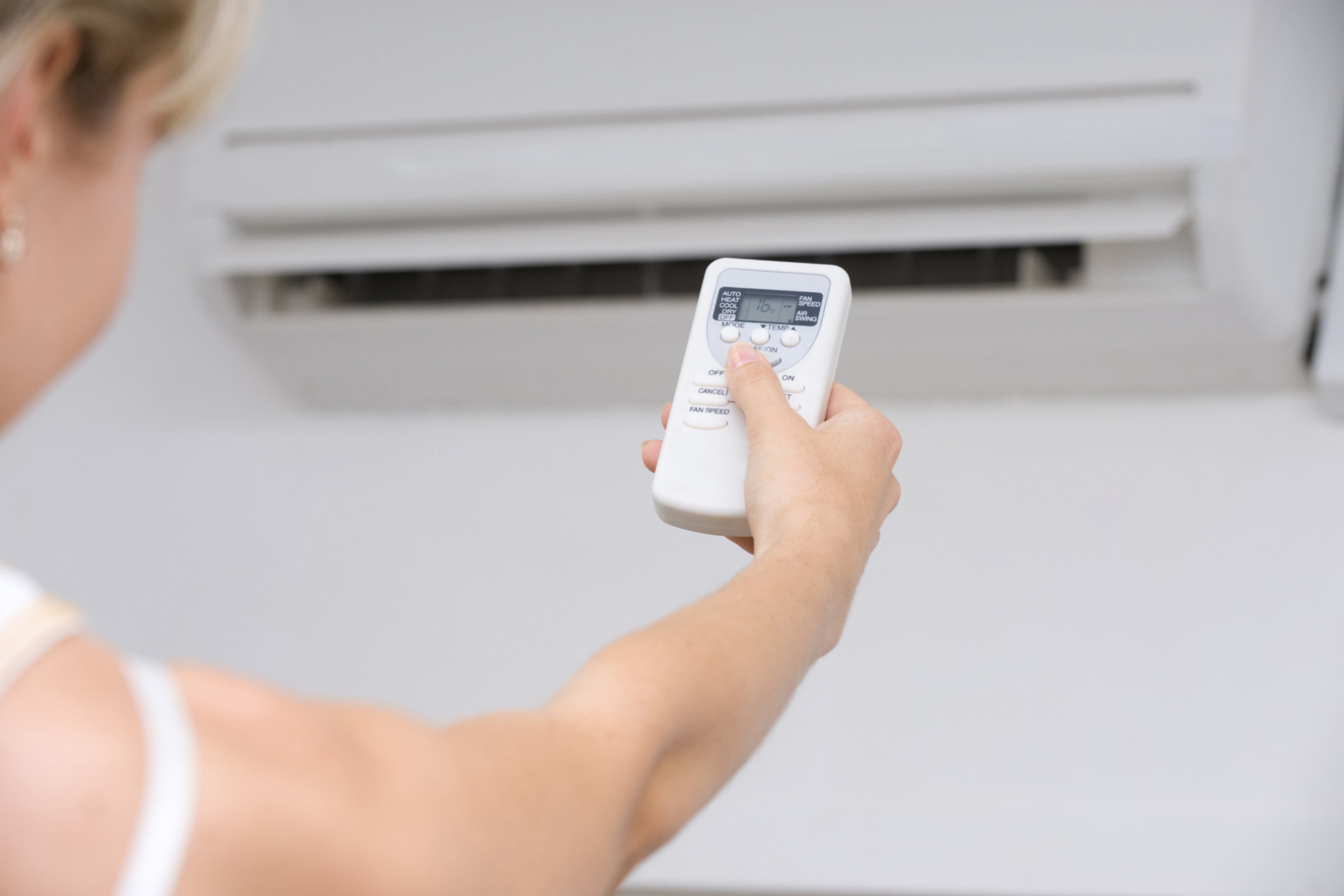 Hand met airco afstandsbediening. Airco lager zetten bespaart energie.