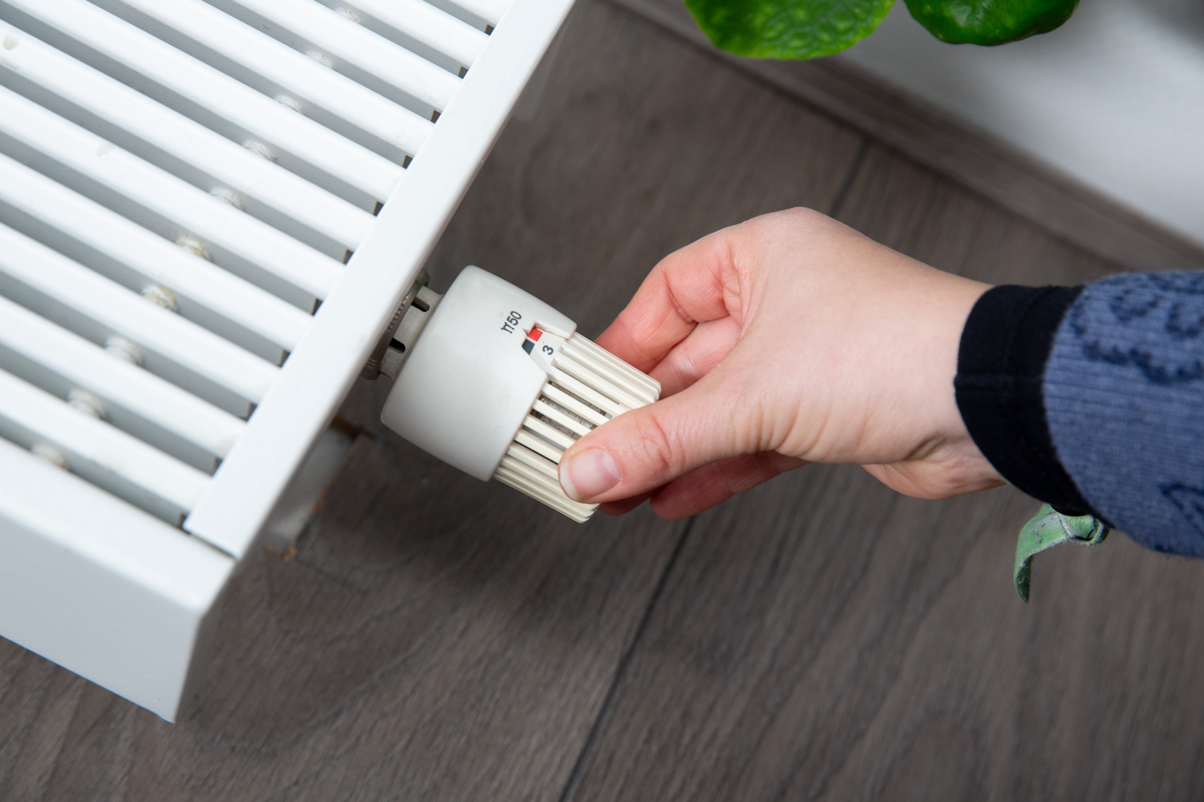 Hand bij thermostaatknop. Goed instellen thermostaat bespaart energie.