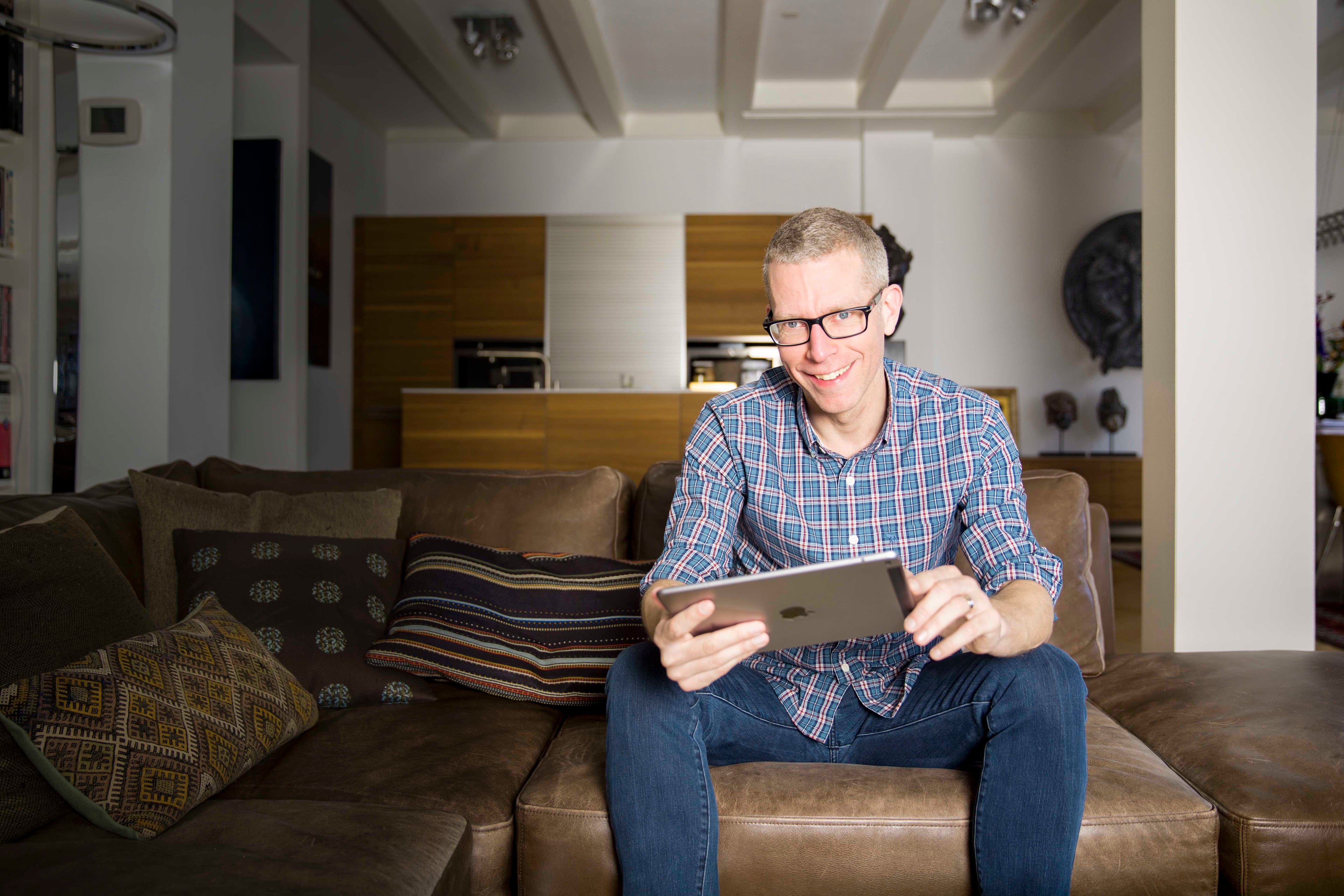 Man op bank met ipad waarop hij zijn energieverbruik in huis afleest.