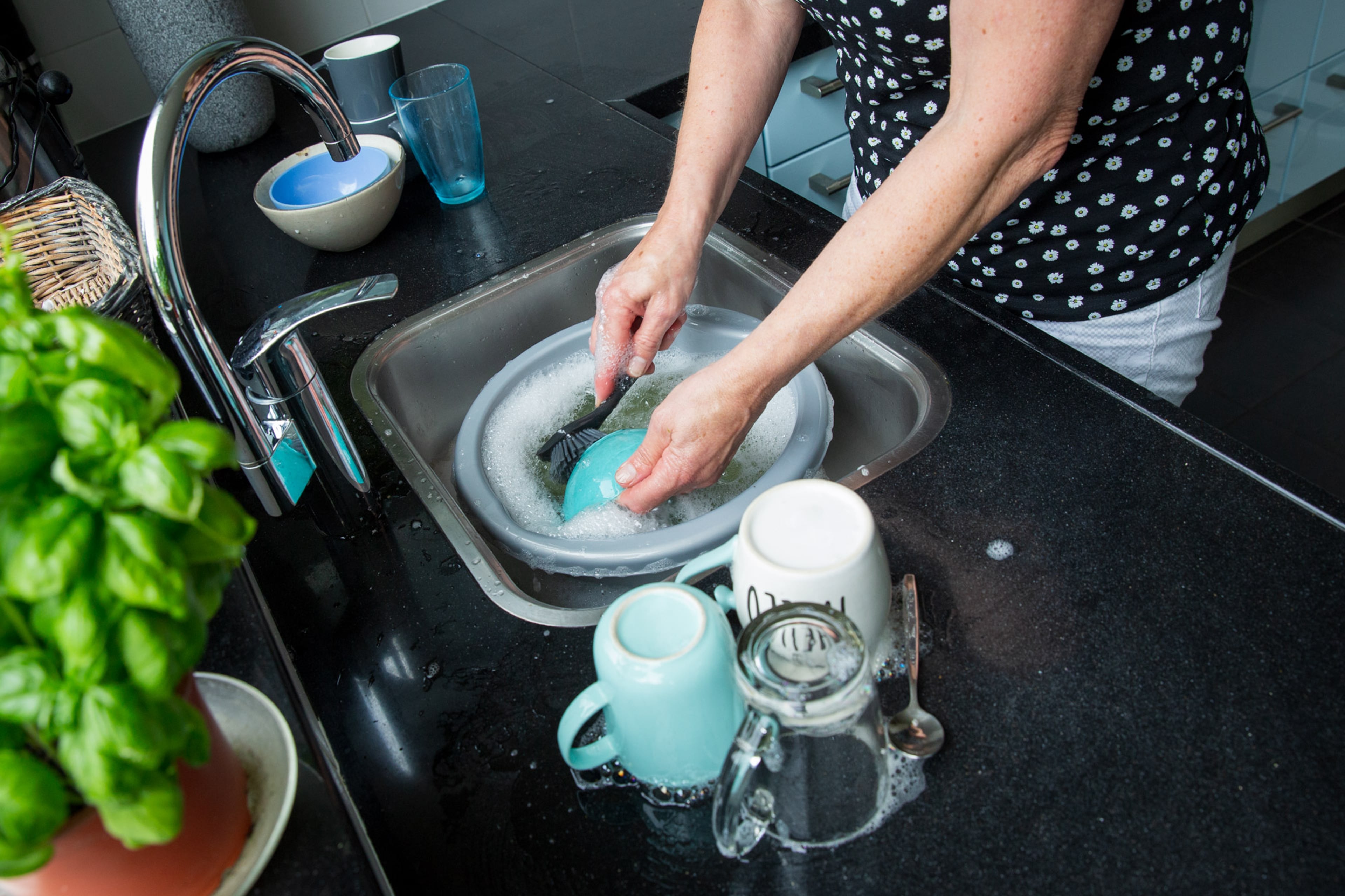 Vrouw doet de vaatwas in een teiltje.