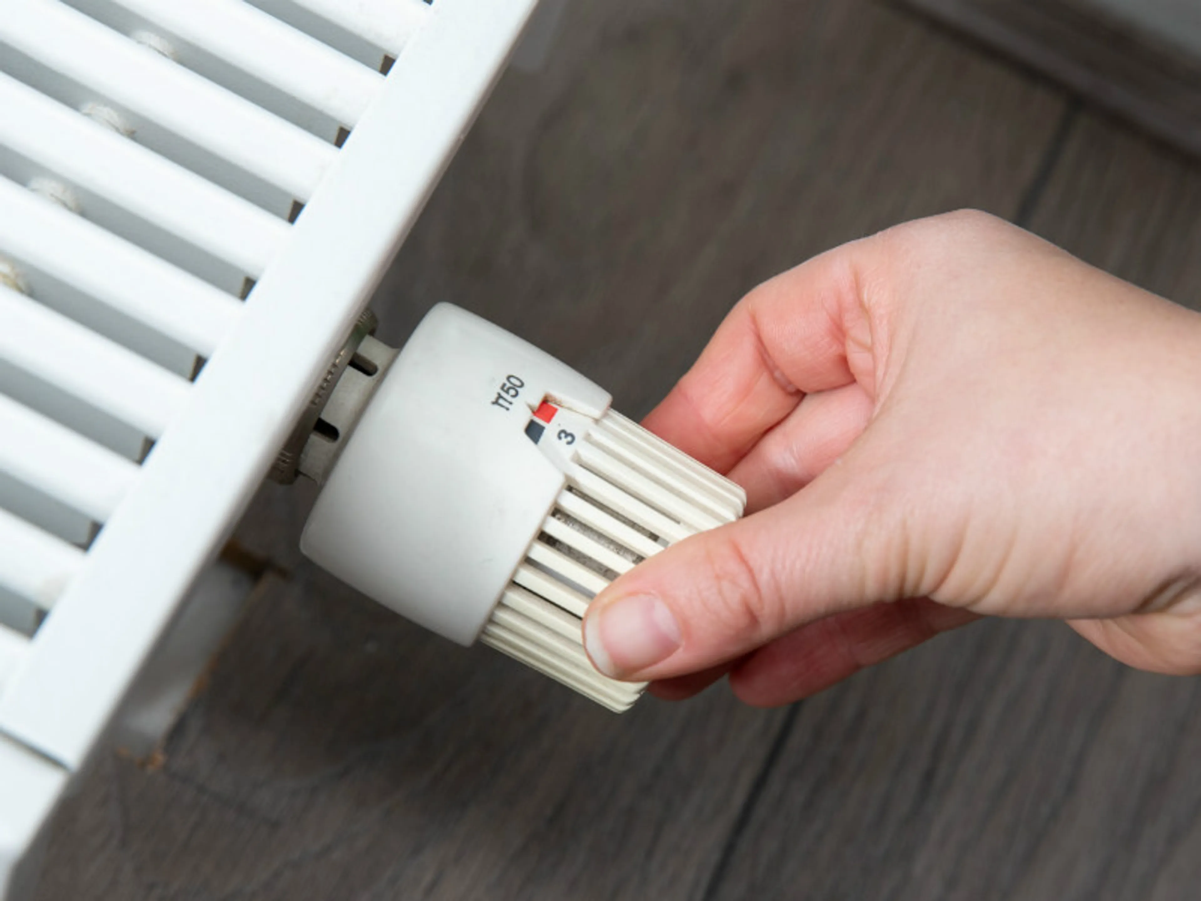 Een hand draait aan een thermostaatknop. In elke ruimte moet je de temperatuur kunnen regelen.