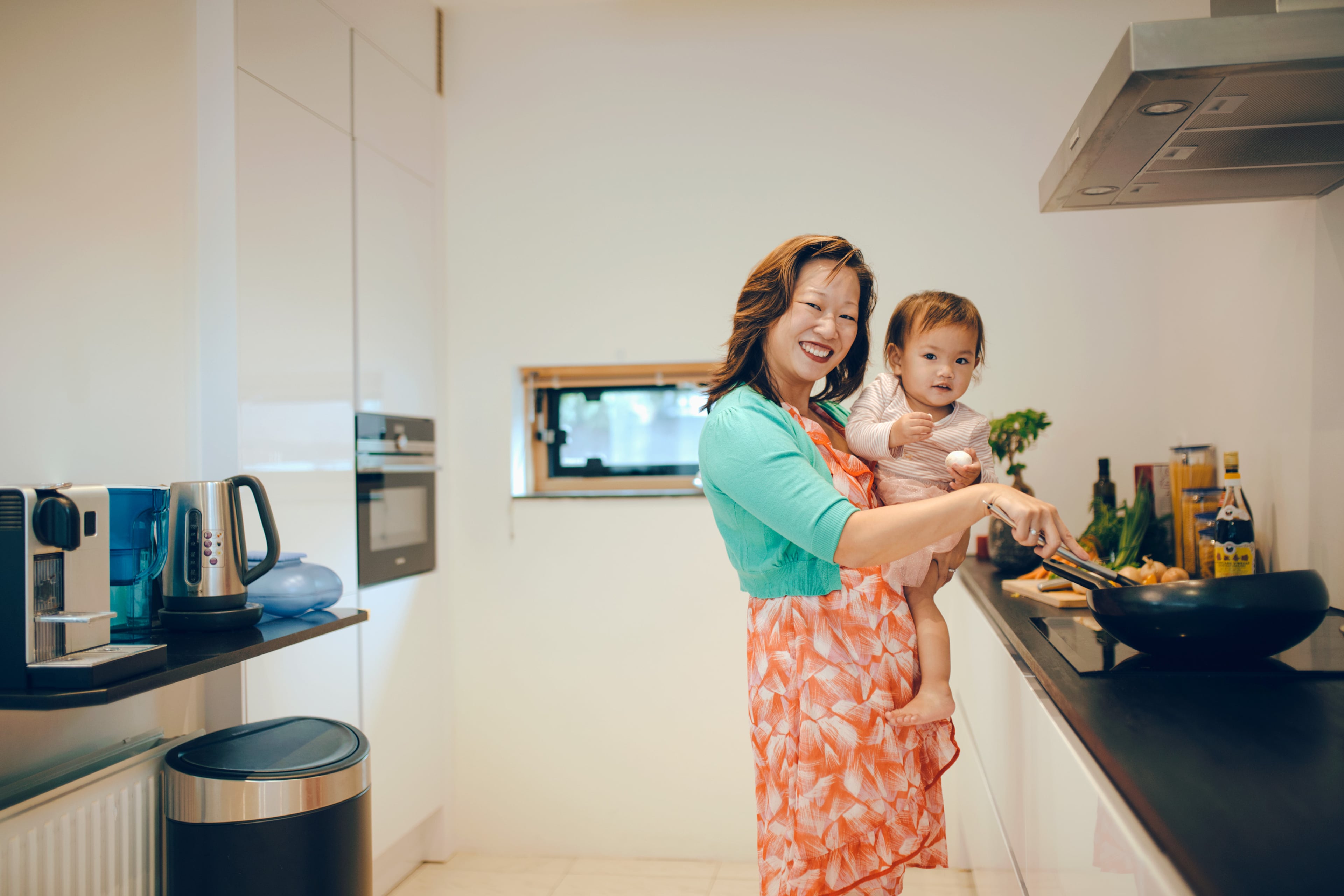 Moeder met kind op de heup aan het koken op inductiekookplaat.