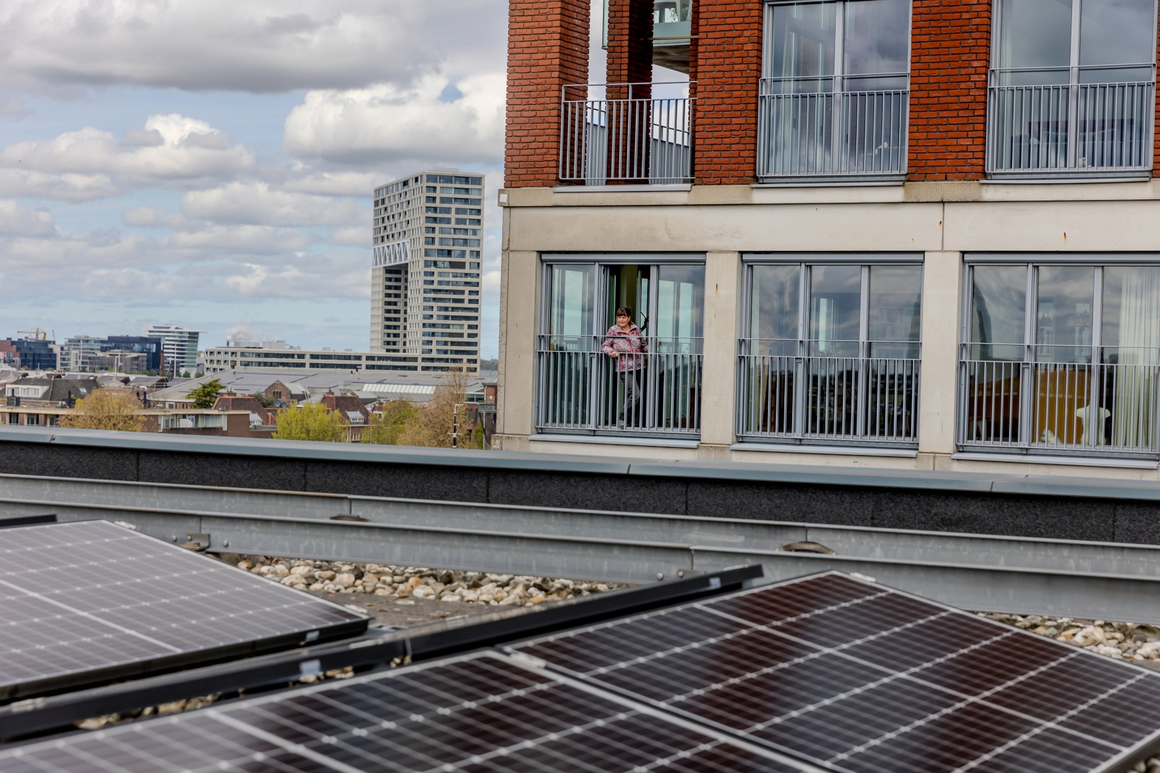 Vrouw kijkt vanaf haarl balkon naar zonnepanelen op een platdak