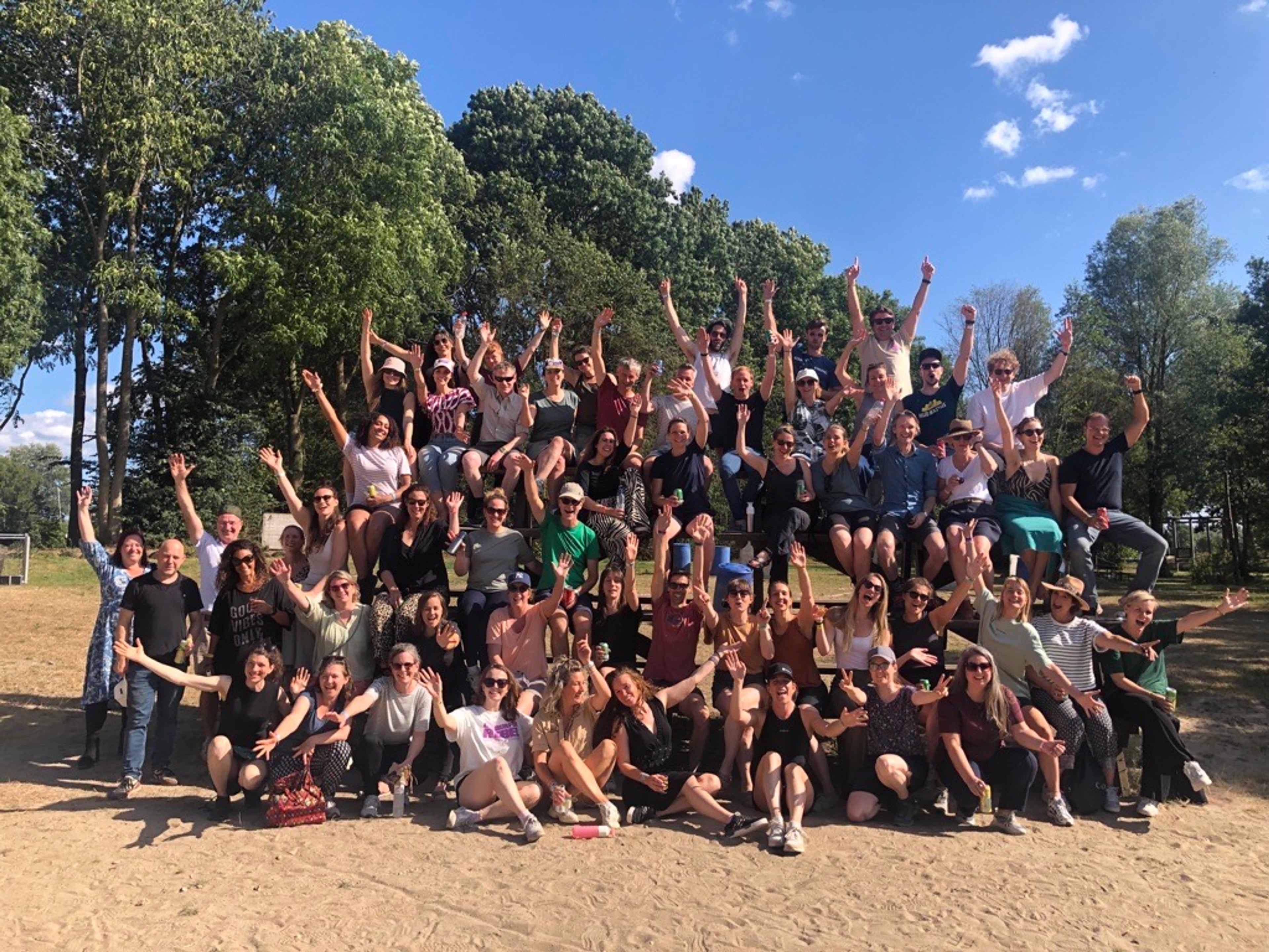 Groepsfoto van de medewerkers van Milieu Centraal in de zomer van 2025. De groep is op een strand en op de achtergrond zijn bomen te zien.